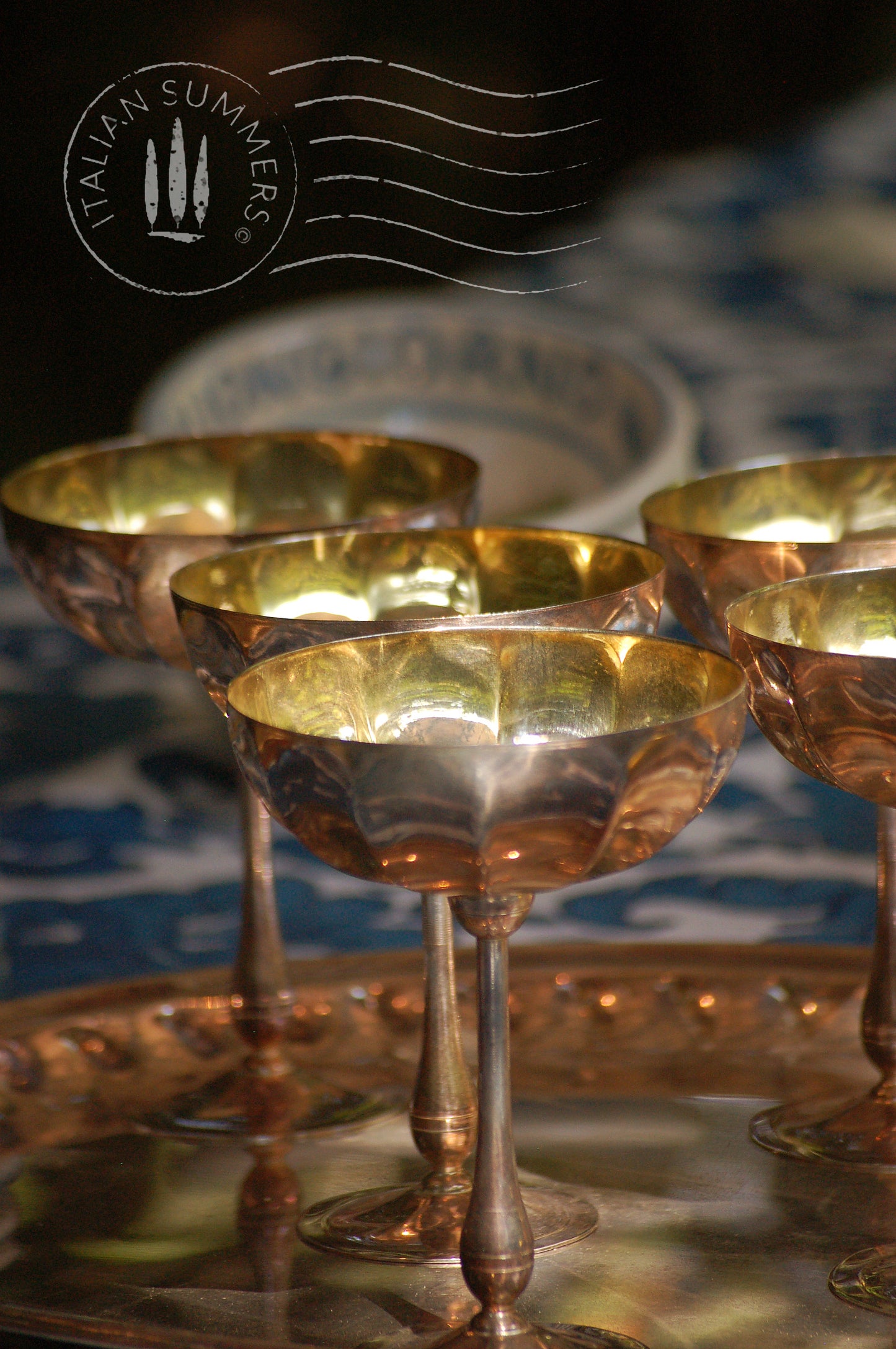 Italian Vintage Champagne coupes.set of six silver and gold plated long stemmed coupes on a silver plated tray upon a table with a flower blue Mediterranean pattern. A bowls with lemons is nearby along with white and blue maiolica serving bowls.,