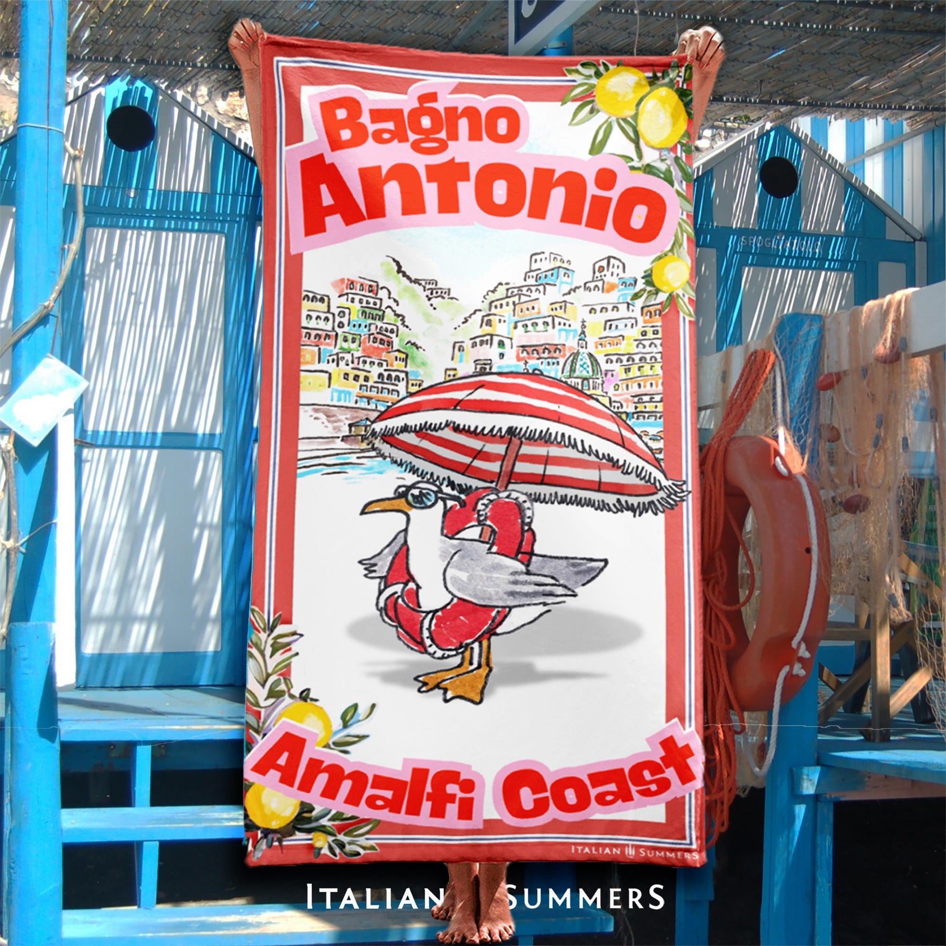 Illustrated Amalfi Coast beach towel featuring a funny seagull wearing sunglasses and a life saver while standing under a striped beach umbrella, Positano in the background, and vintage lemon borders with the text Bagno Antonio and Amalfi Coast Designed by Italian Summers