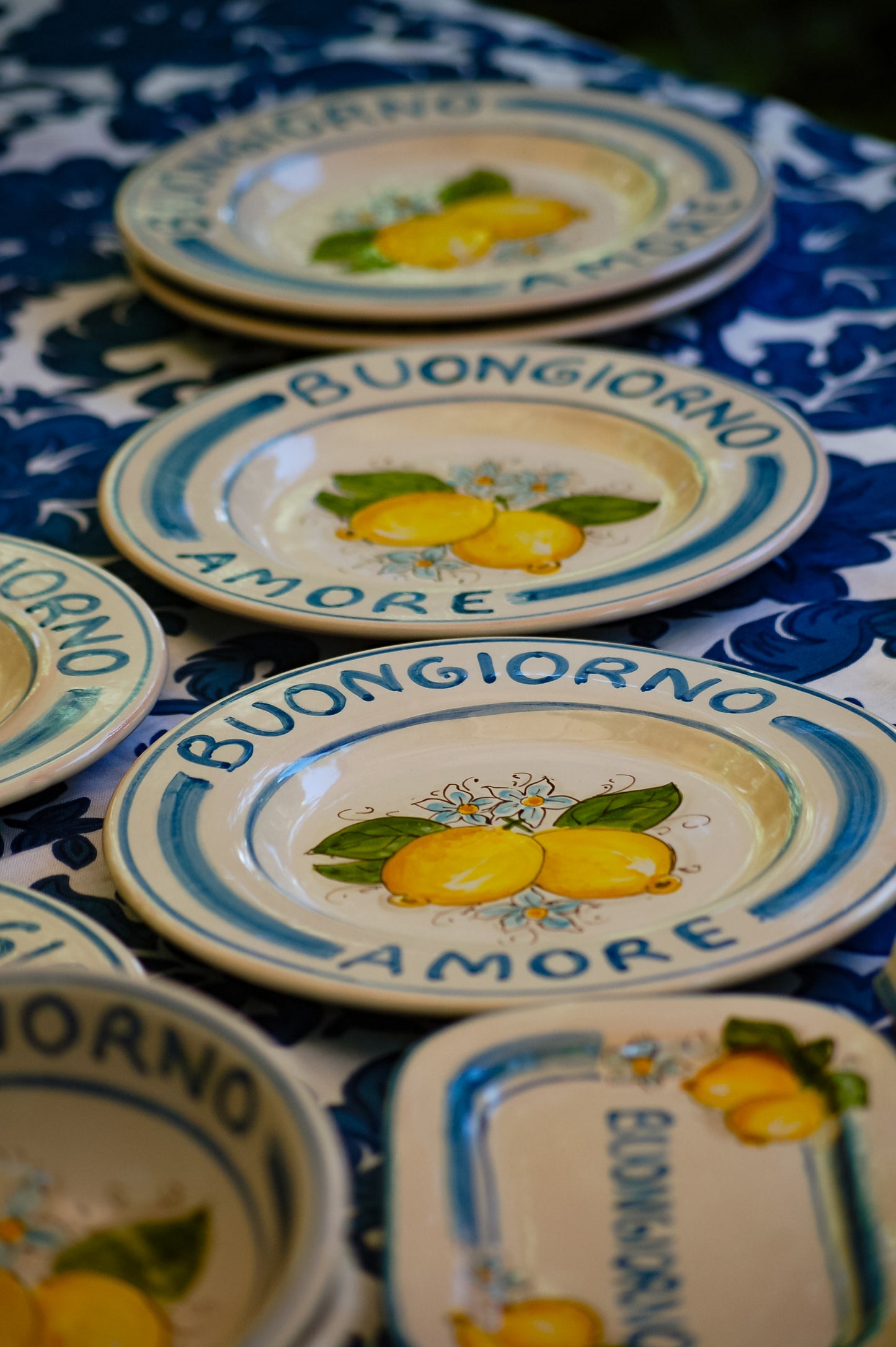 A bright and colorful Maiolica ceramic plate, hand made in Sicily featuring sunny Sicilian lemons and a blue decoration with the text, Buongiorno Amore, which means, Good Morning my Love in Italian.