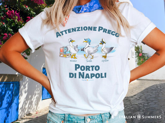 A cotton T-Shirt with the Italian text PORTO di NAPOLI in blue block letters and featuring the hand-drawn sketches of  three seagulls dressed up as a sailor, a tourist, and a boat captain.
