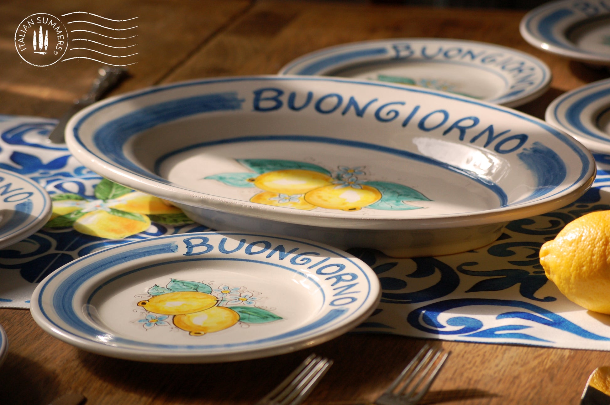 Ceramic plate Buongiorno Limoni handpainted in Sicily. This plate has the quote Biongiorno on the rim - handpainted - And colorfull lemons on the center of the plate with lemon flowers. On the rim of the plate there are blue paint stripes. The blue color is ultra marine. This plate is designed and sold by Italian Summers.