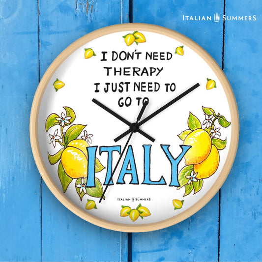 Italy inspired wall clock with the quote "I don't need therapy, I just need to go to Italy" . The quote is in the top center of the clock in balck handriting. In the lower part of the clock there is Italy written in big blue letter with on both sides a bundle of lemons with flowers. In stead of numbers there are little lemons. The body if the clock is available in wood color and white. The hands color is available in white and black. Made by Italian Summers.