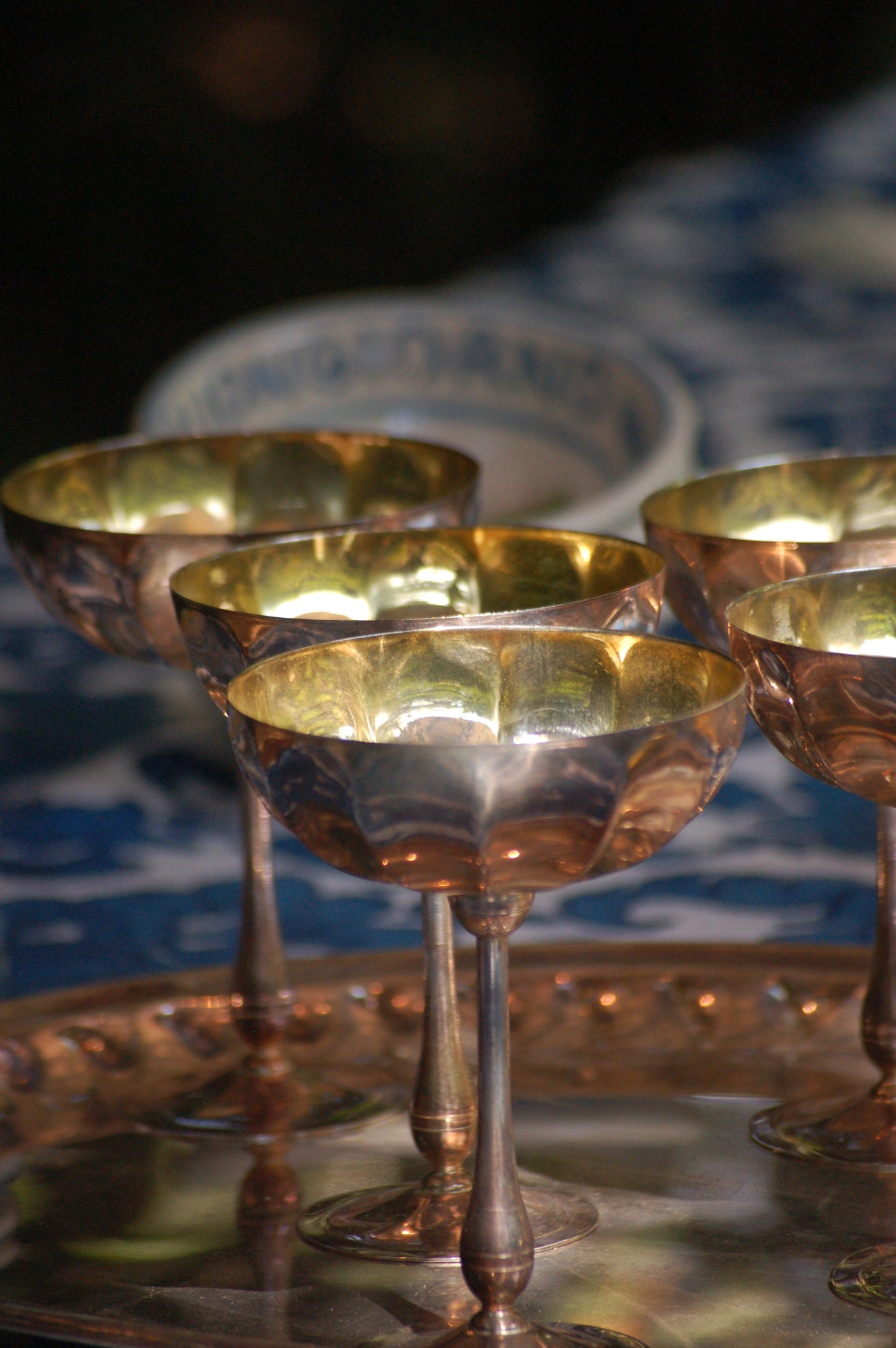 Italian Vintage Champagne coupes.set of six silver and gold plated long stemmed coupes on a silver plated tray upon a table with a flower blue Mediterranean pattern. A bowls with lemons is nearby along with white and blue maiolica serving bowls.,