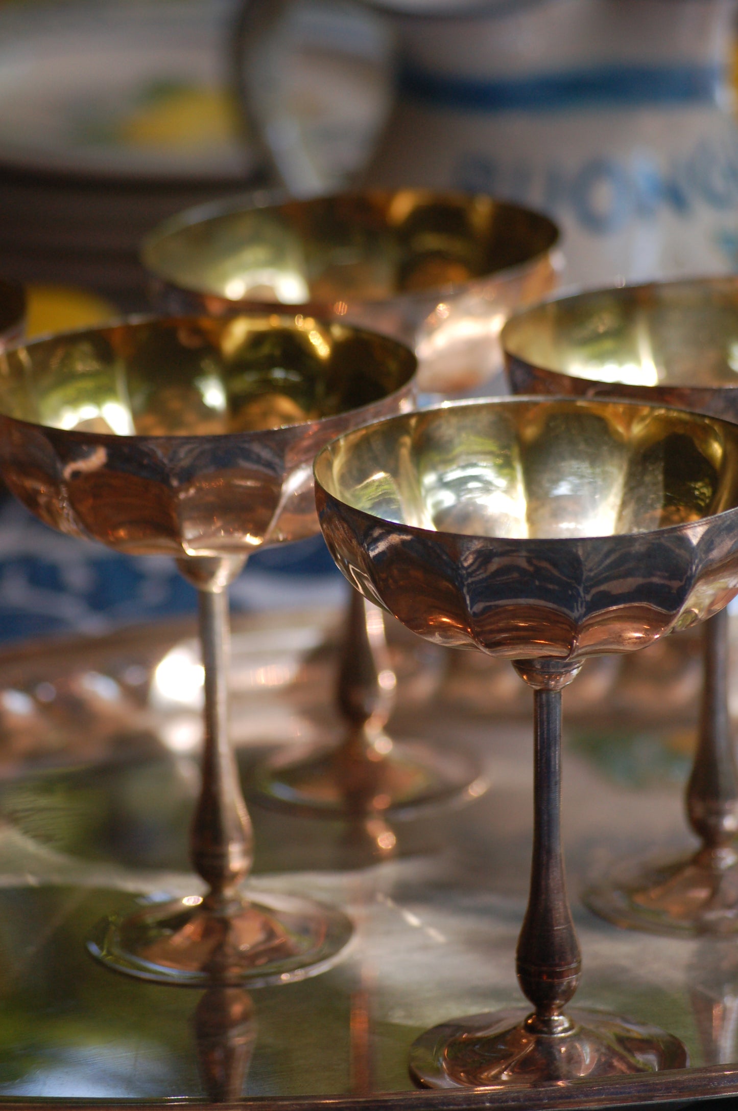 Italian Vintage Champagne coupes.set of six silver and gold plated long stemmed coupes on a silver plated tray upon a table with a flower blue Mediterranean pattern. A bowls with lemons is nearby along with white and blue maiolica serving bowls.,