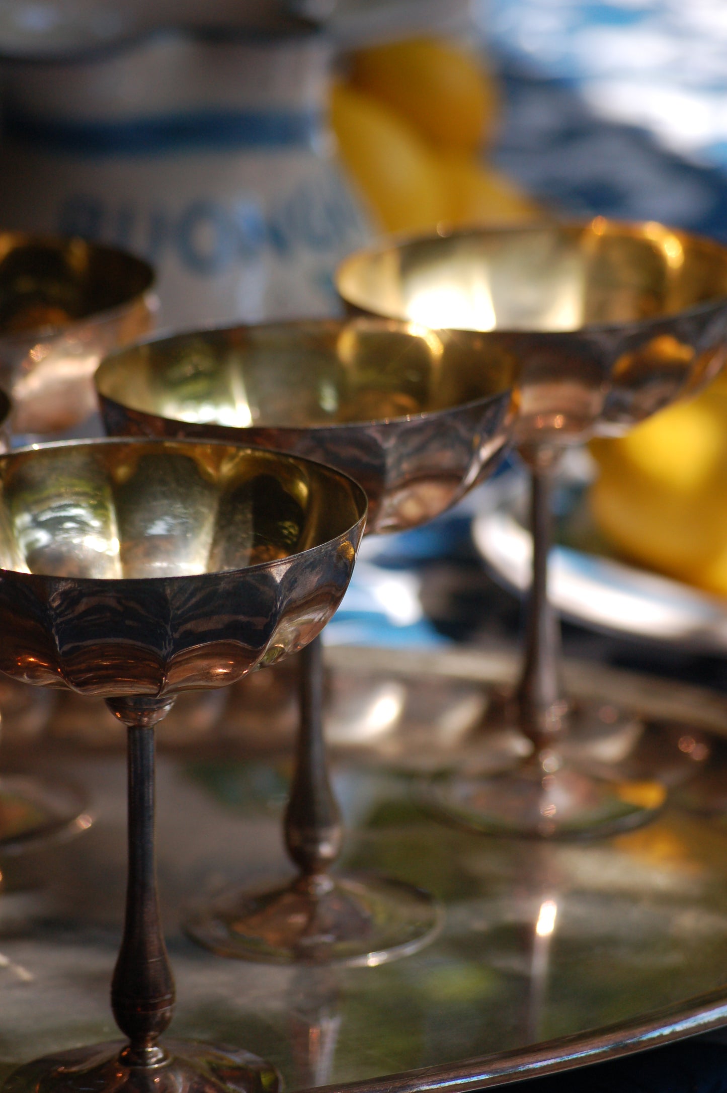 Italian Vintage Champagne coupes.set of six silver and gold plated long stemmed coupes on a silver plated tray upon a table with a flower blue Mediterranean pattern. A bowls with lemons is nearby along with white and blue maiolica serving bowls.,