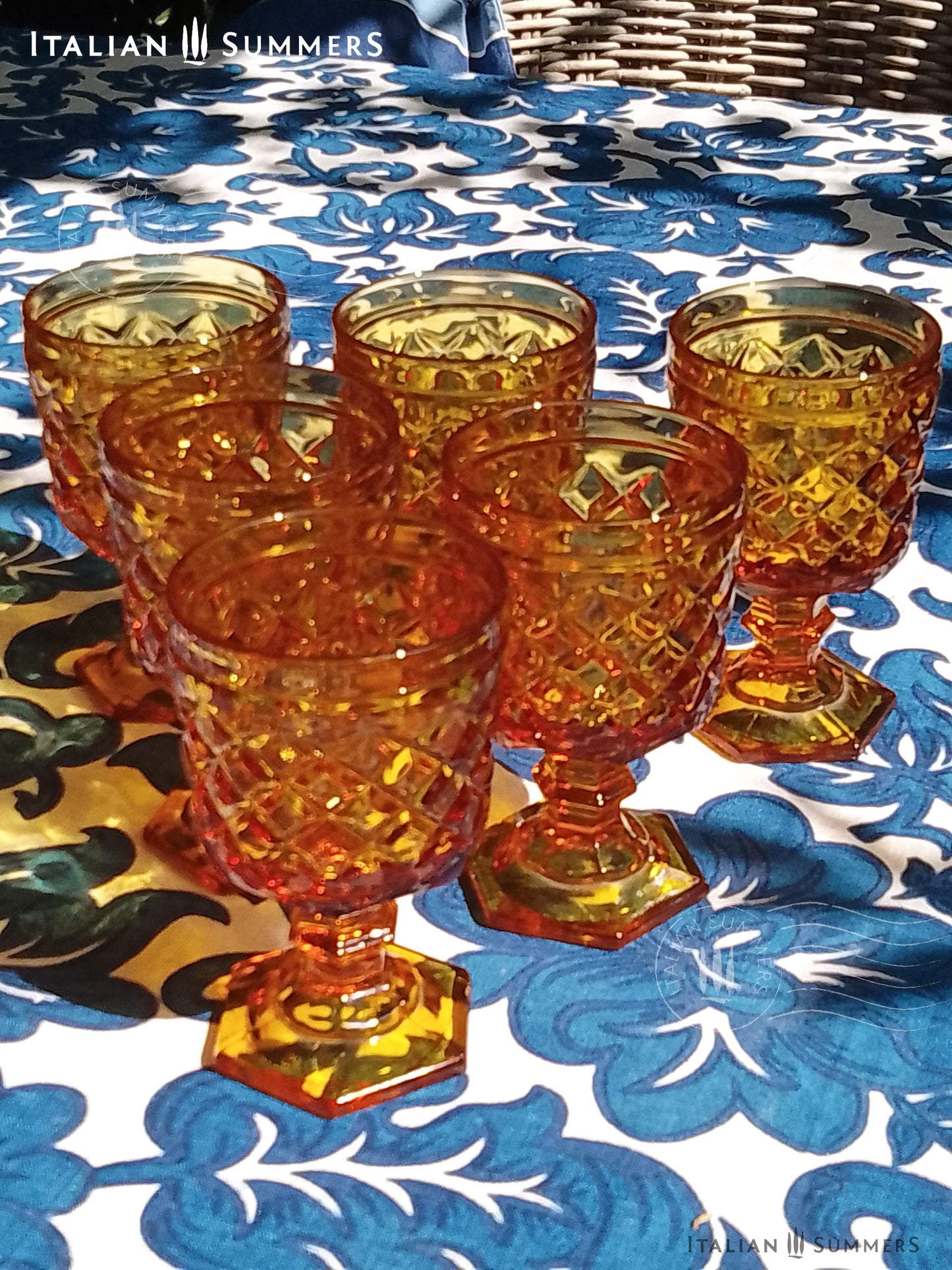 Set of Italian amber glass goblets and a carafe with the original Bormioli box on a floral patterned tablecloth.