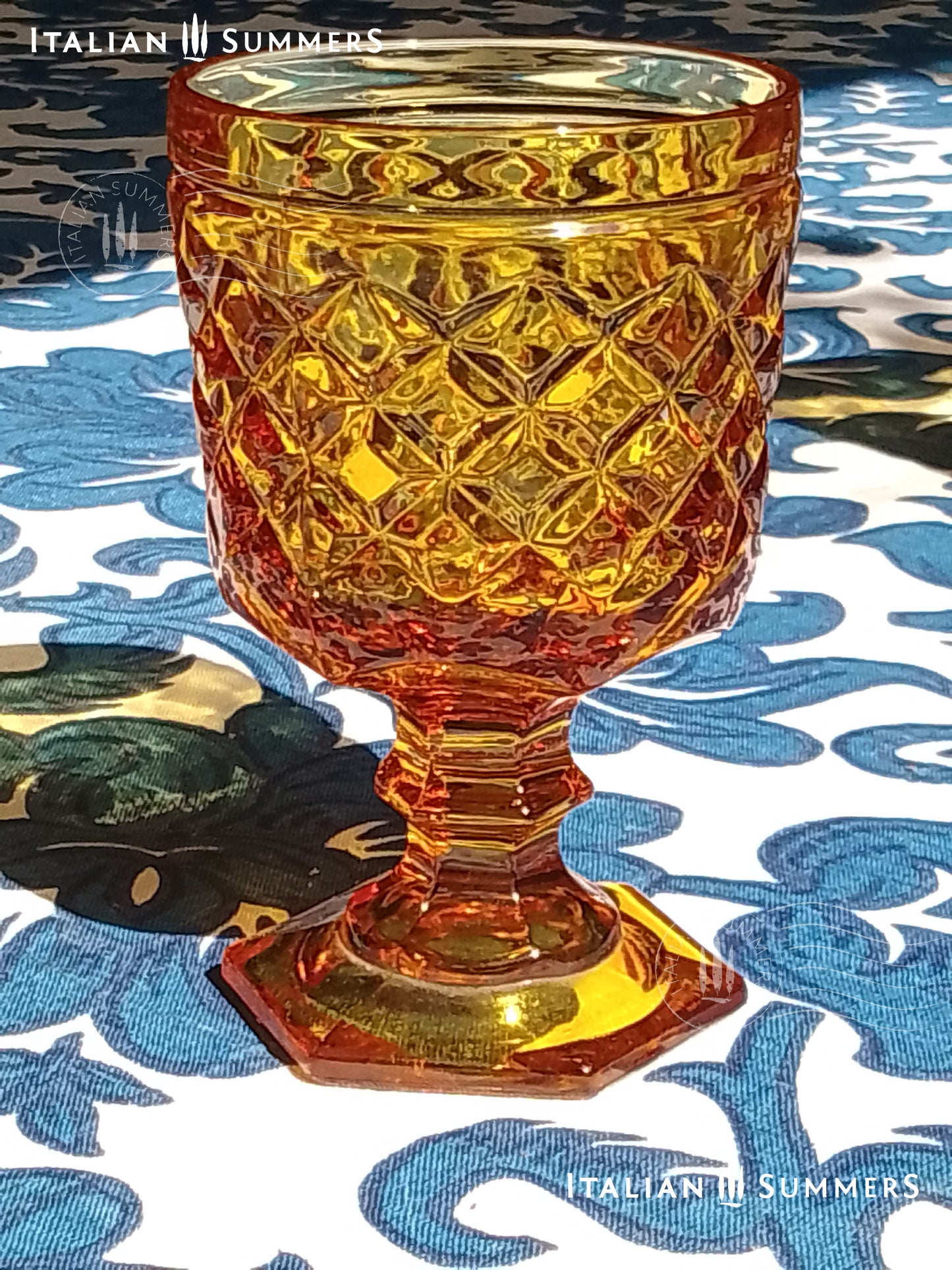 Set of Italian amber glass goblets and a carafe with the original Bormioli box on a floral patterned tablecloth.