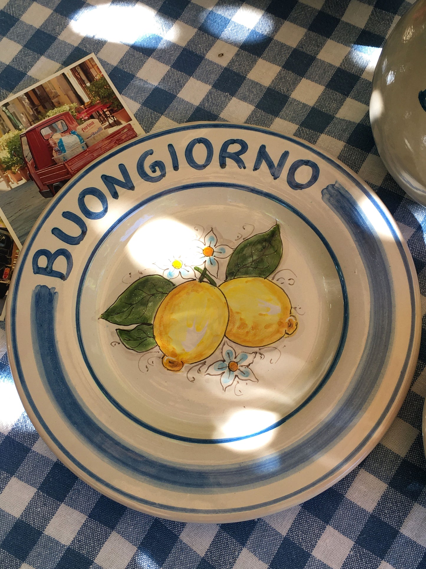 Ceramic plate Buongiorno Limoni handpainted in Sicily. This plate has the quote Biongiorno on the rim - handpainted - And colorfull lemons on the center of the plate with lemon flowers. On the rim of the plate there are blue paint stripes. The blue color is ultra marine. This plate is designed and sold by Italian Summers.