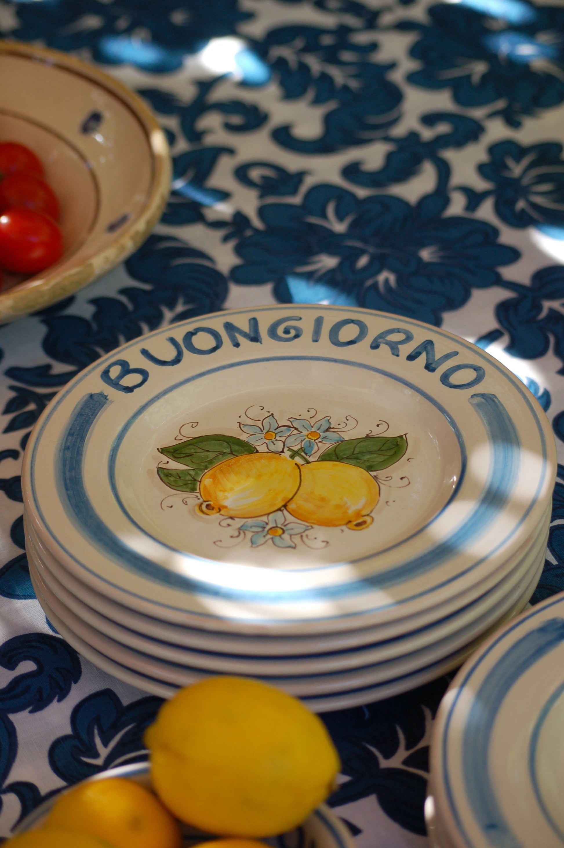 Ceramic plate Buongiorno Limoni handpainted in Sicily. This  plate has the quote Biongiorno on the rim - handpainted  - And colorfull lemons on the center of the plate  with lemon flowers. On the rim of the plate there are blue paint stripes. The blue color is ultra marine. This plate is designed and sold by Italian Summers.