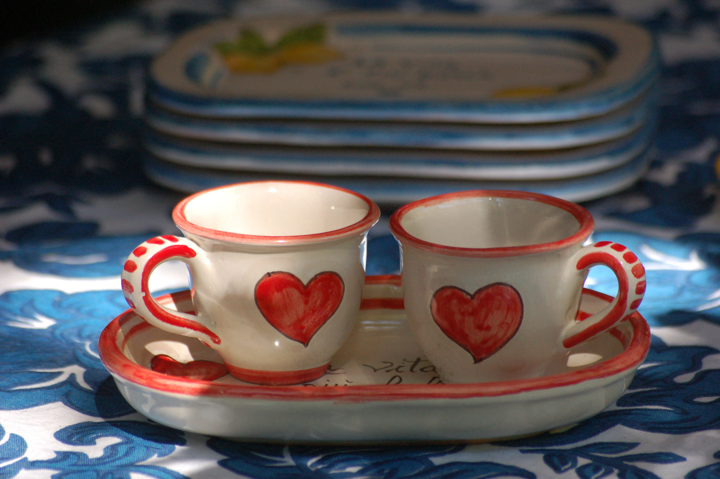 A bright and colorful Italian Maiolica ceramic espresso coffee set, two demitasse and a serving tray featuring happy Sicilian red hearts and a decoration with the Italian text -La vita e' piu bella con te-. hand made in Sicily