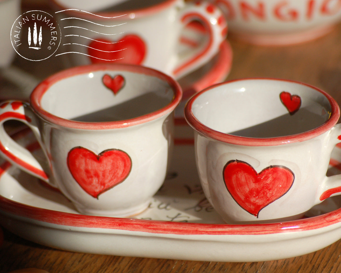 A bright and colorful Italian Maiolica ceramic espresso coffee set, two demitasse and a serving tray featuring happy Sicilian red hearts and a decoration with the Italian text -La vita e' piu bella con te-. hand made in Sicily