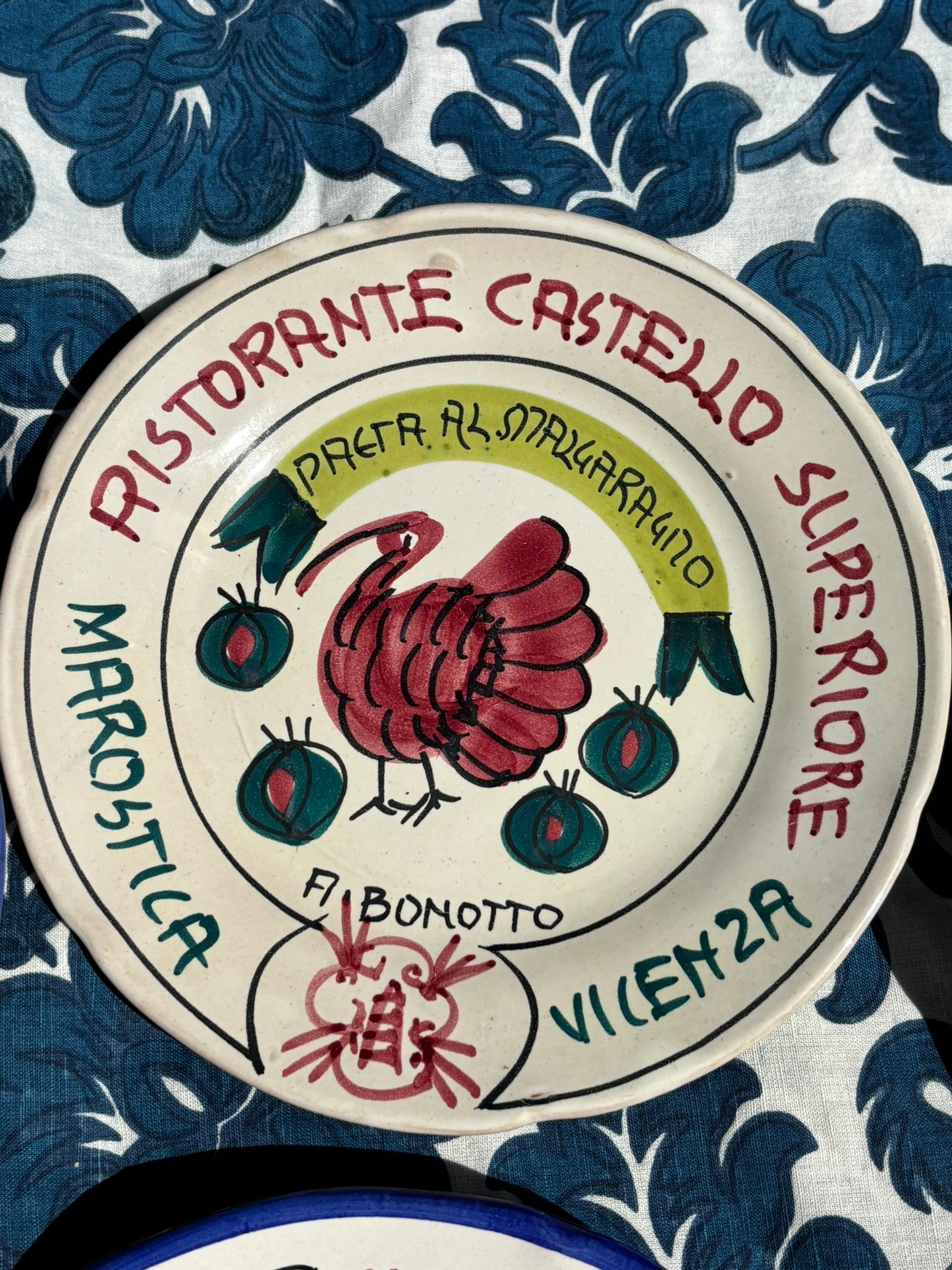 Italian ceramic plate with 'Ristorante Castello Superiore' Vicenza text and a turkey design on a blue floral tablecloth