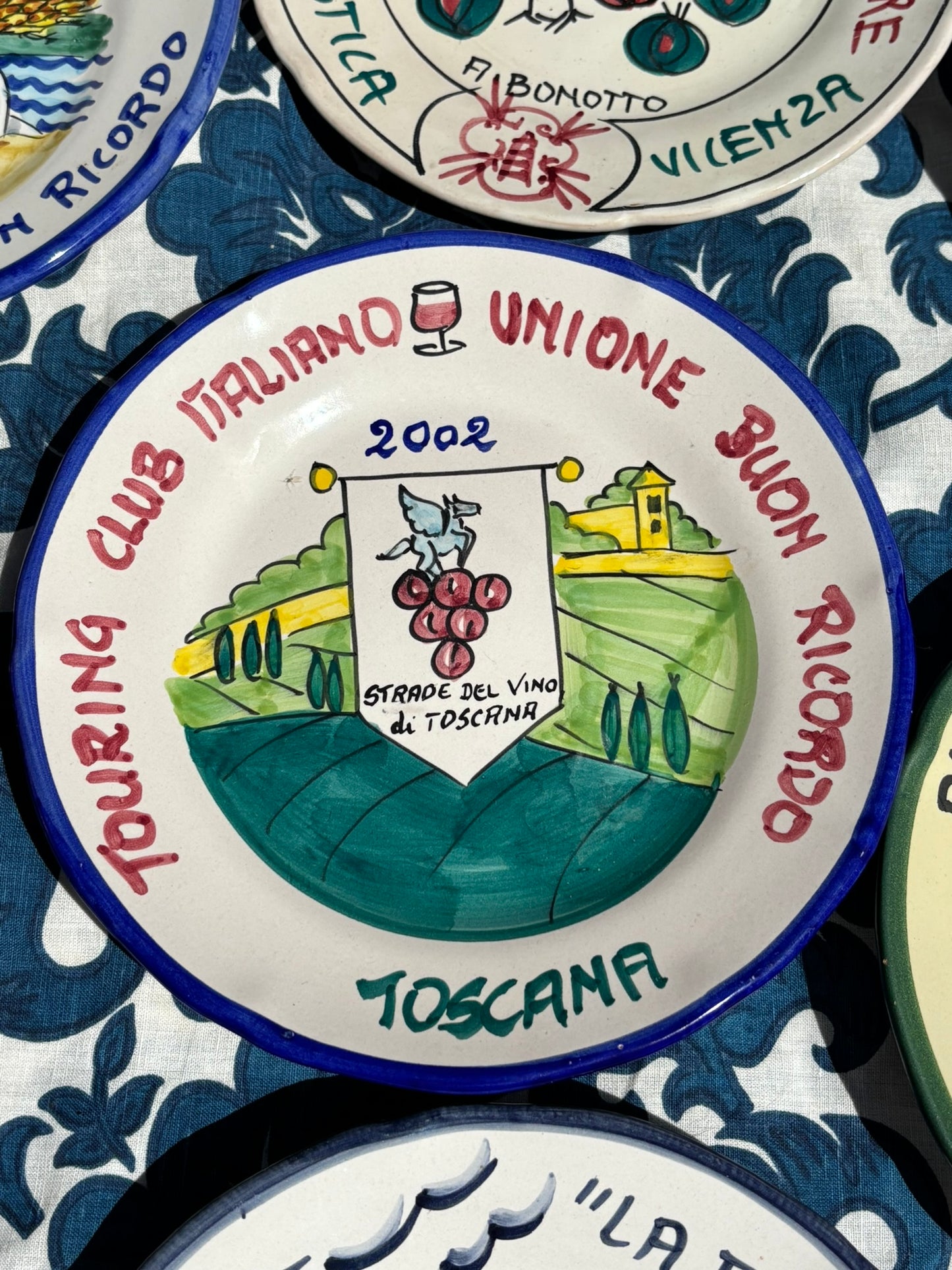 Italian ceramic plate with Italian text Touring Club Italiano Toscana and handpainted graphics of Tuscany on white and blue patterned background