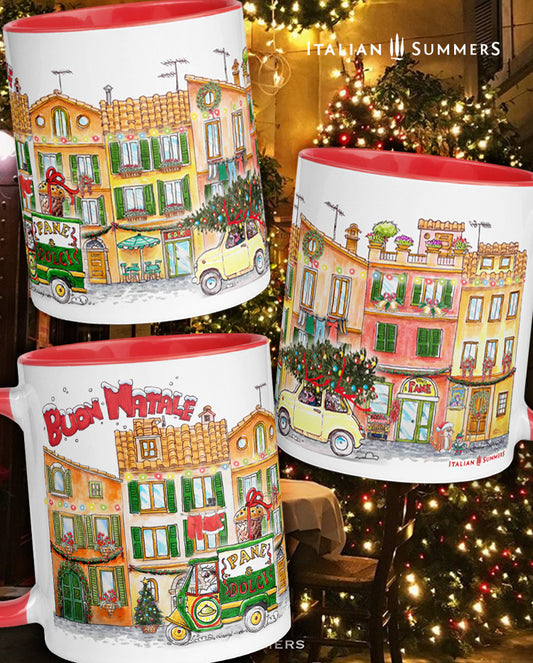 Christmas mug VILLAGGIO di NATALE designed and sold by Italian Summers. A Christmas mug with Italian houses in a row in terracotta colors and green shutters in Chirstmas time. A typical streetscene from an Italian village during Christmas time. There is laundry hanging, there are christmas lights and Christmas trees, the baker in his car with a big panettone, an a family in a vintage 500 with a Christmas tree on the roof. There is the text Buon Natale in red. 