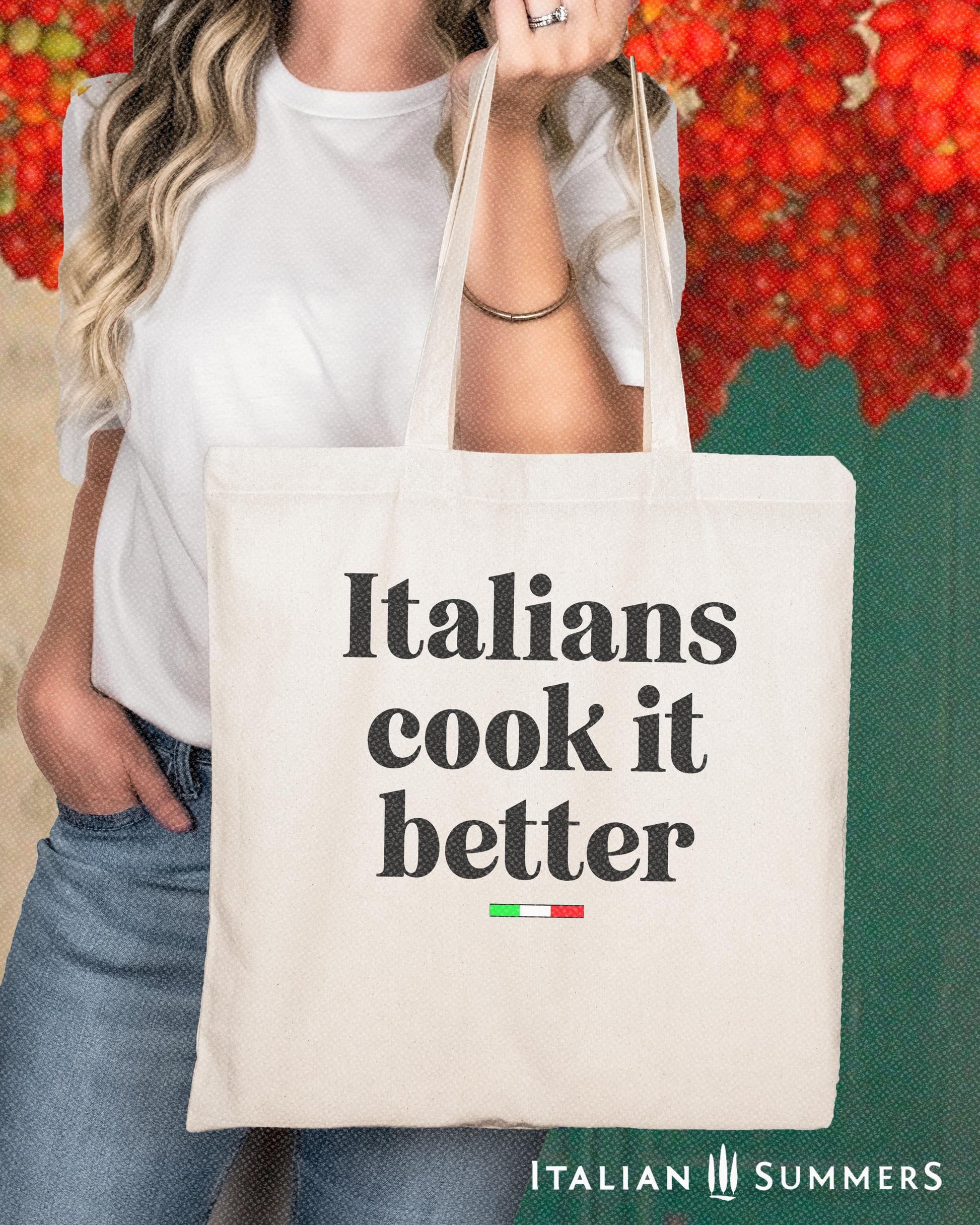 A Canvas tote bag with the quote Italians cook it better. Under the text in a black font there is a little bar with the happy colors of the Italian flag.  in the background is a  shady Italian terrace with hanging tomatoes.  By Italian Summers
