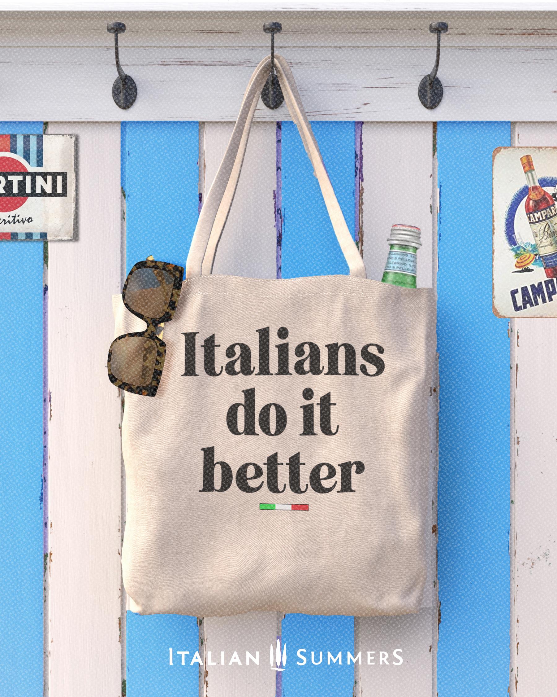 A Canvas tote bag with the quote Italians do it better. Under the text in a black font there is a little bar with the happy colors of the Italian flag.  in the background is a white and blue wooden striped wall, a bottle of Italian mineral water and some sunglasses stick out of the tote bag. Designed by Italian Summers