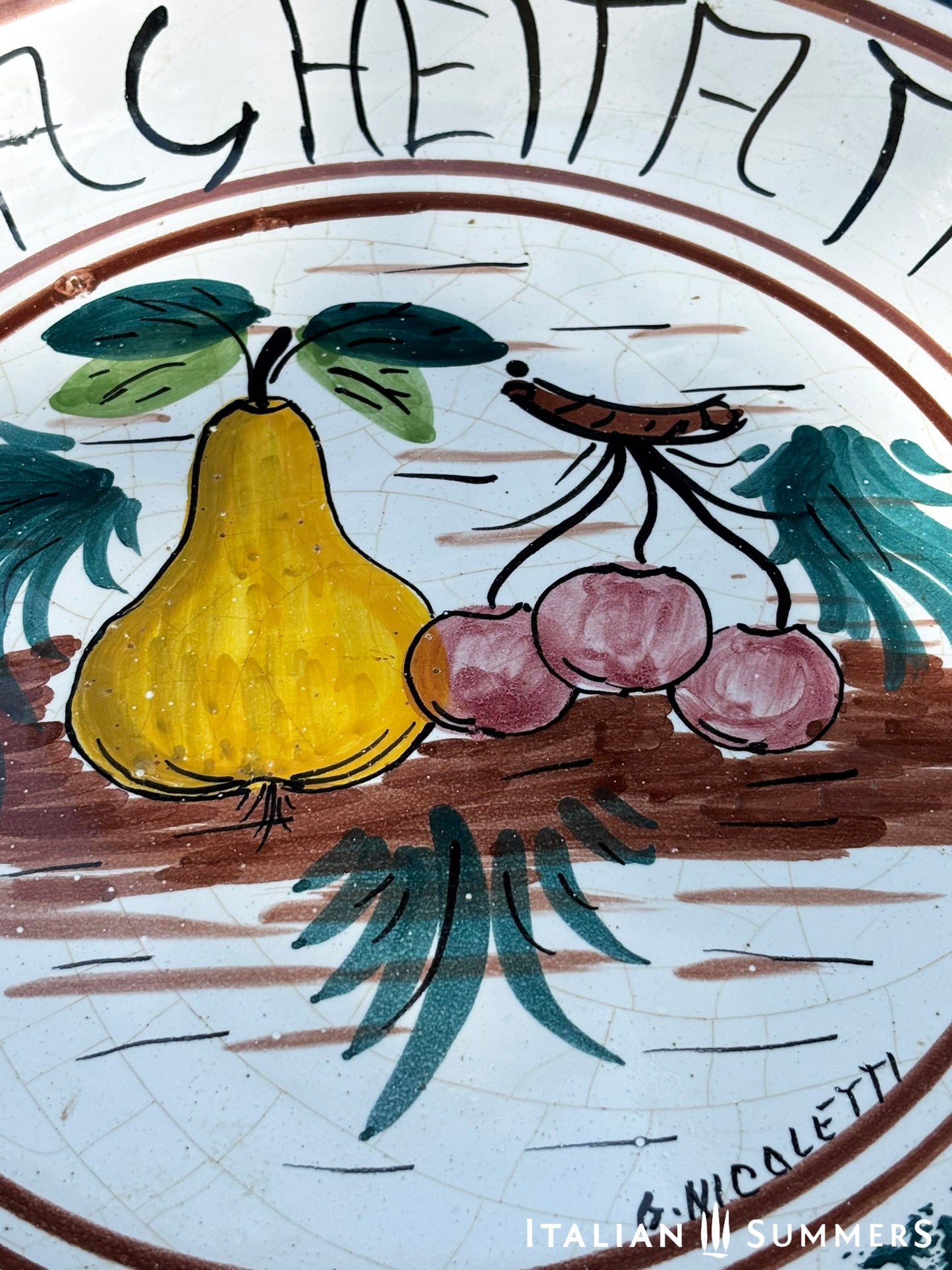 A large Sicilian vintage serving or Decorative plate with 'Spaghettata"' text and pear and cherries traditional Sicilian Maiolica illustration, on a blue floral patterned background.