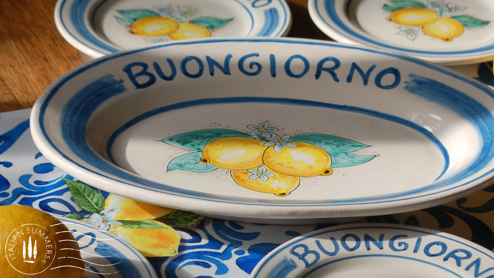 Ceramic plate Buongiorno Limoni handpainted in Sicily. This plate has the quote Biongiorno on the rim - handpainted - And colorfull lemons on the center of the plate with lemon flowers. On the rim of the plate there are blue paint stripes. The blue color is ultra marine. This plate is designed and sold by Italian Summers.