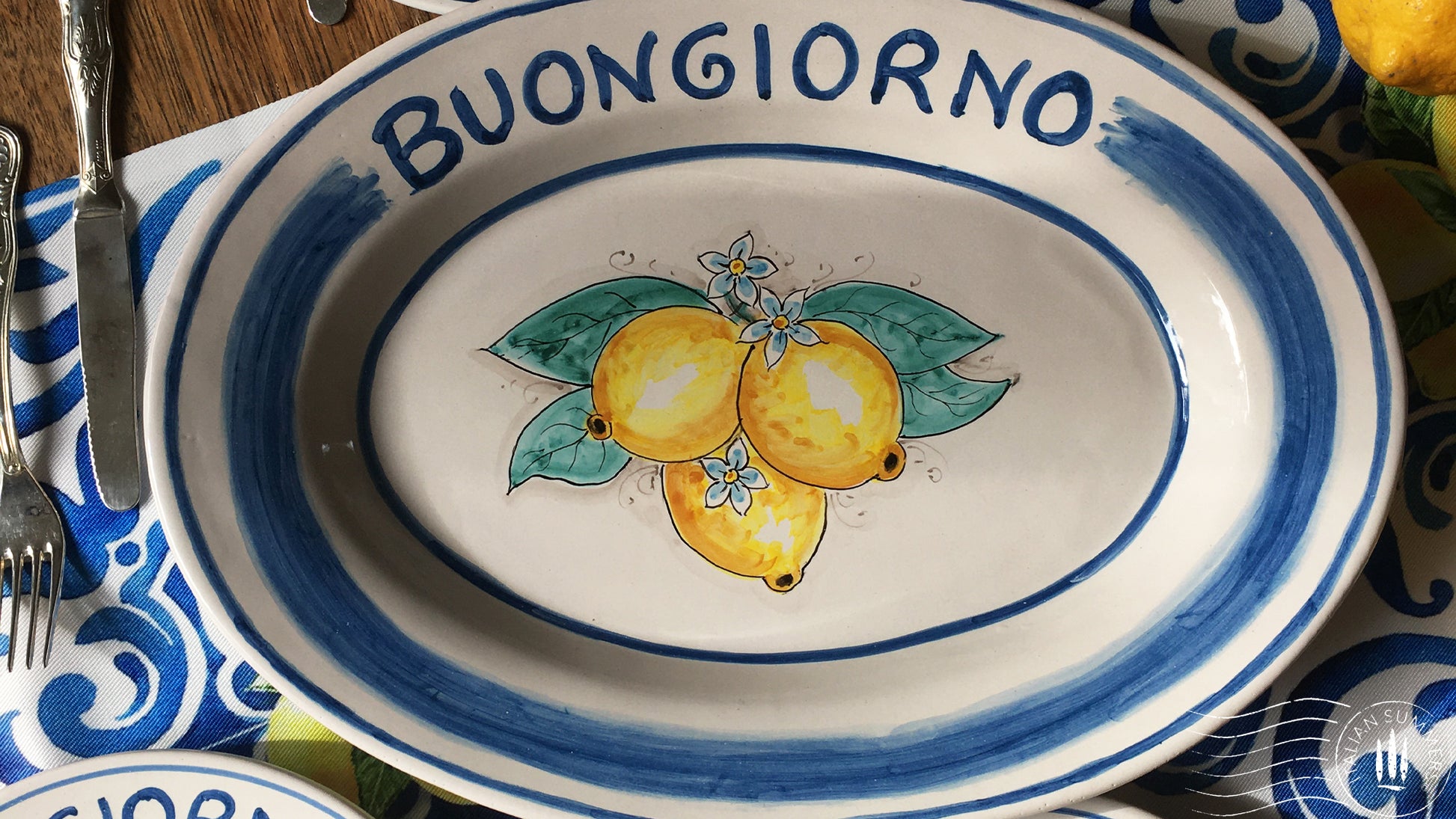 Ceramic plate Buongiorno Limoni handpainted in Sicily. This plate has the quote Biongiorno on the rim - handpainted - And colorfull lemons on the center of the plate with lemon flowers. On the rim of the plate there are blue paint stripes. The blue color is ultra marine. This plate is designed and sold by Italian Summers.