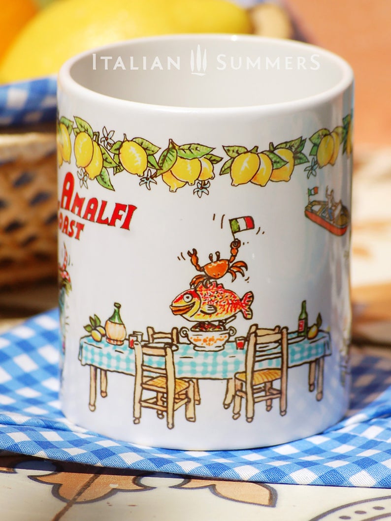Italy | Amalfi Coast inspired mug with sketches that refer to the Amalfi Coast | Positano. There is a light blue vintage Cinquecento cabrio with a man and a woman seen from the back, the colorful houses of the Amalfi coast, a long table with a blue checkered table cloth, lemons, wine, a smiling fish and a crab with an Italian flag. On the rim there is a lemon garland and in the middle the red writing Amalfi coast. A really happy mug! Made by Italian Summers