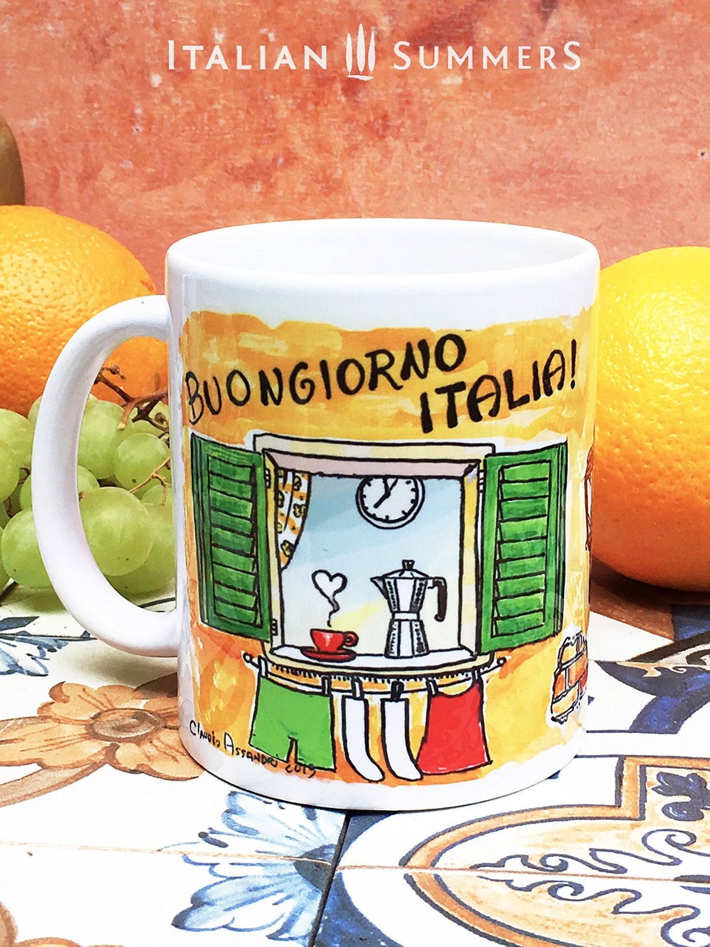 Italy inspired mug by sketches of an open Italian window. The window has green shutter, on the lower part of the windows hangs laundry in the color of the Italian flag. In the window sill ther is a red coffee mug and an Italian coffee poet, la moka. The Italian window is surrounded by a terracotta wall. Above the window there is written 'Buongiorno Italia' in black handwriting. Made by Italian Summers