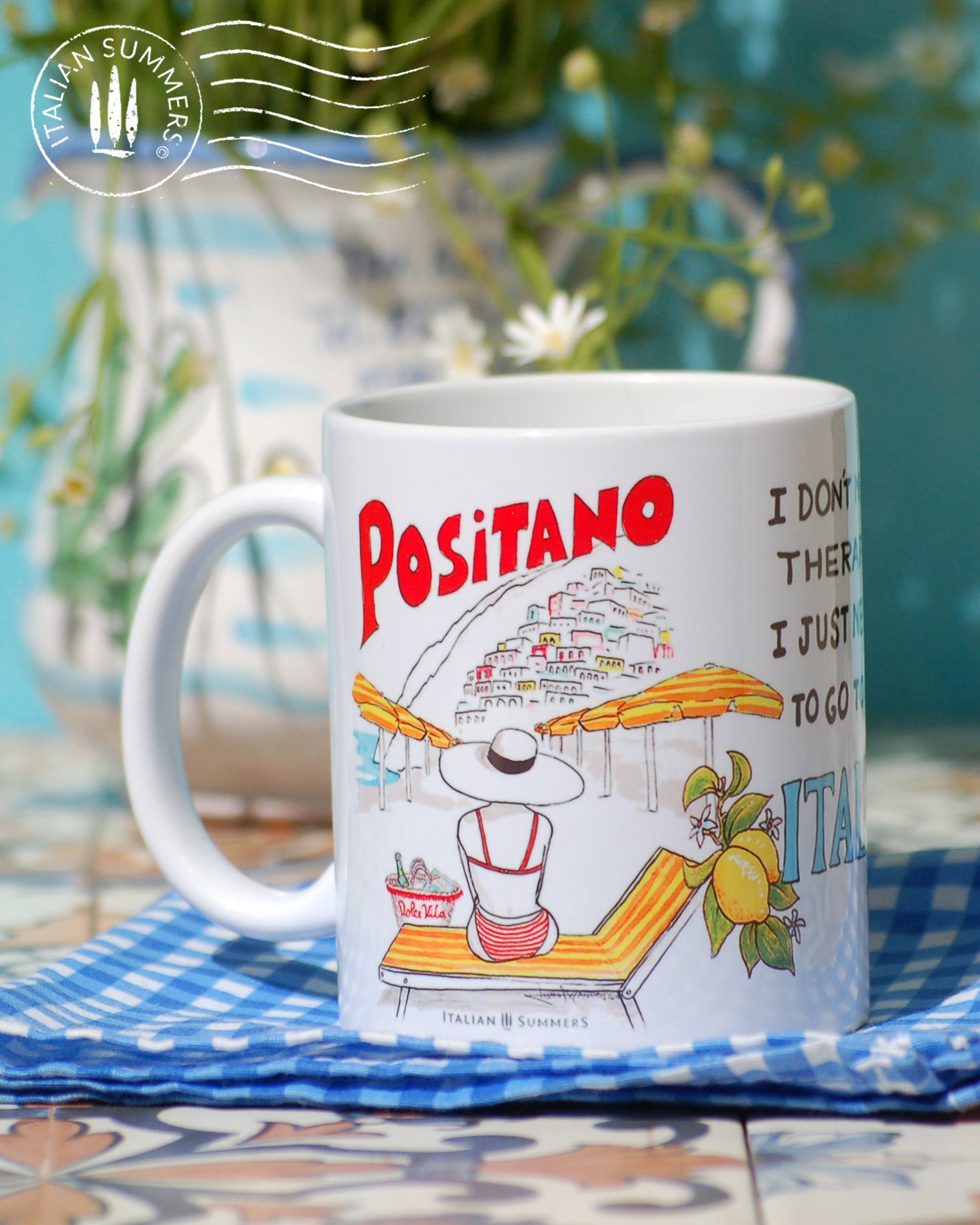 Mug inspired by Positano with a sketch of Positano beach with the yellow orange beach umbrellas and a view and on Positano. There is a lady sittng on a striped beach bed, she wears a hat and has a straw bag with Dolce Vita written on it. This sketch is on tweo sides of the mug and in the center there is the quote I don't need therapy, I just need to go to Italy. There is also Positano written on the mug is red above the village of Positano. The quote is decorated with lemons.