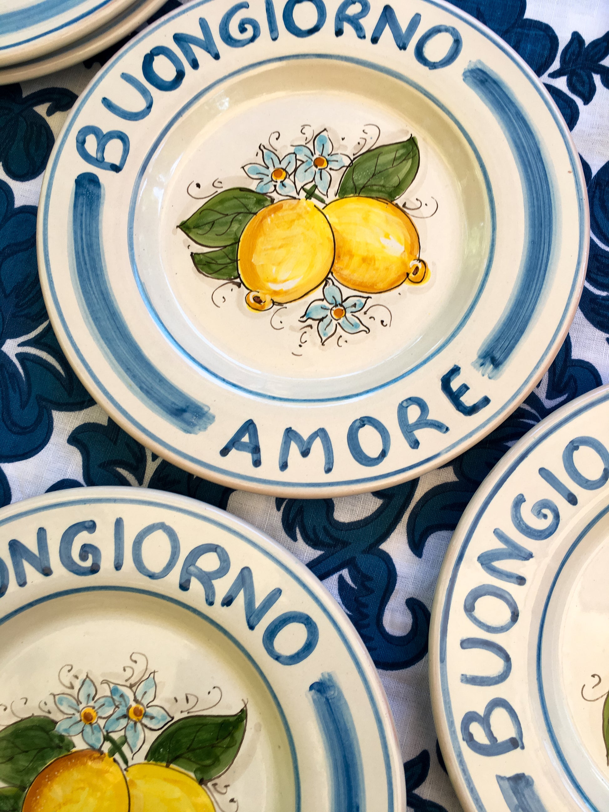 A bright and colorful Maiolica ceramic plate, hand made in Sicily featuring sunny Sicilian lemons and a blue decoration with the text, Buongiorno Amore, which means, Good Morning my Love in Italian.