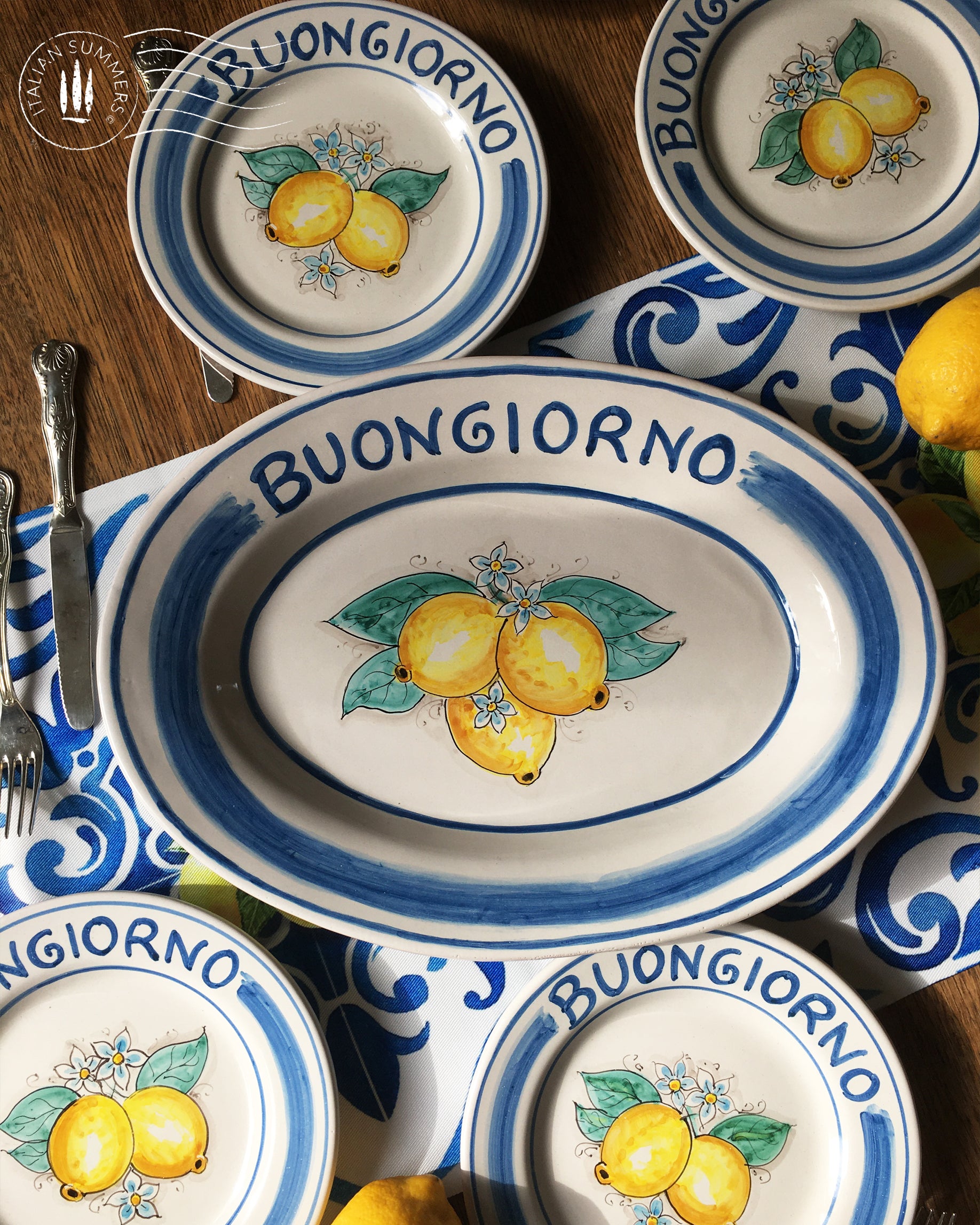Ceramic plate Buongiorno Limoni handpainted in Sicily. This plate has the quote Biongiorno on the rim - handpainted - And colorfull lemons on the center of the plate with lemon flowers. On the rim of the plate there are blue paint stripes. The blue color is ultra marine. This plate is designed and sold by Italian Summers.