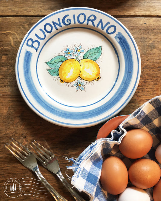 Ceramic plate Buongiorno Limoni handpainted in Sicily. This  plate has the quote Biongiorno on the rim - handpainted  - And colorfull lemons on the center of the plate  with lemon flowers. On the rim of the plate there are blue paint stripes. The blue color is ultra marine. This plate is designed and sold by Italian Summers.