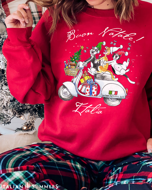 A red Italy-inspired sweatshirt features a large front print of three Italian cats speeding on a vintage Vespa scooter with a load of presents and a asketful of Italian goodies. The cats are singing and the last cat has to hold on as the scooter zooms by. A "Buon Natale" text is printed on top.