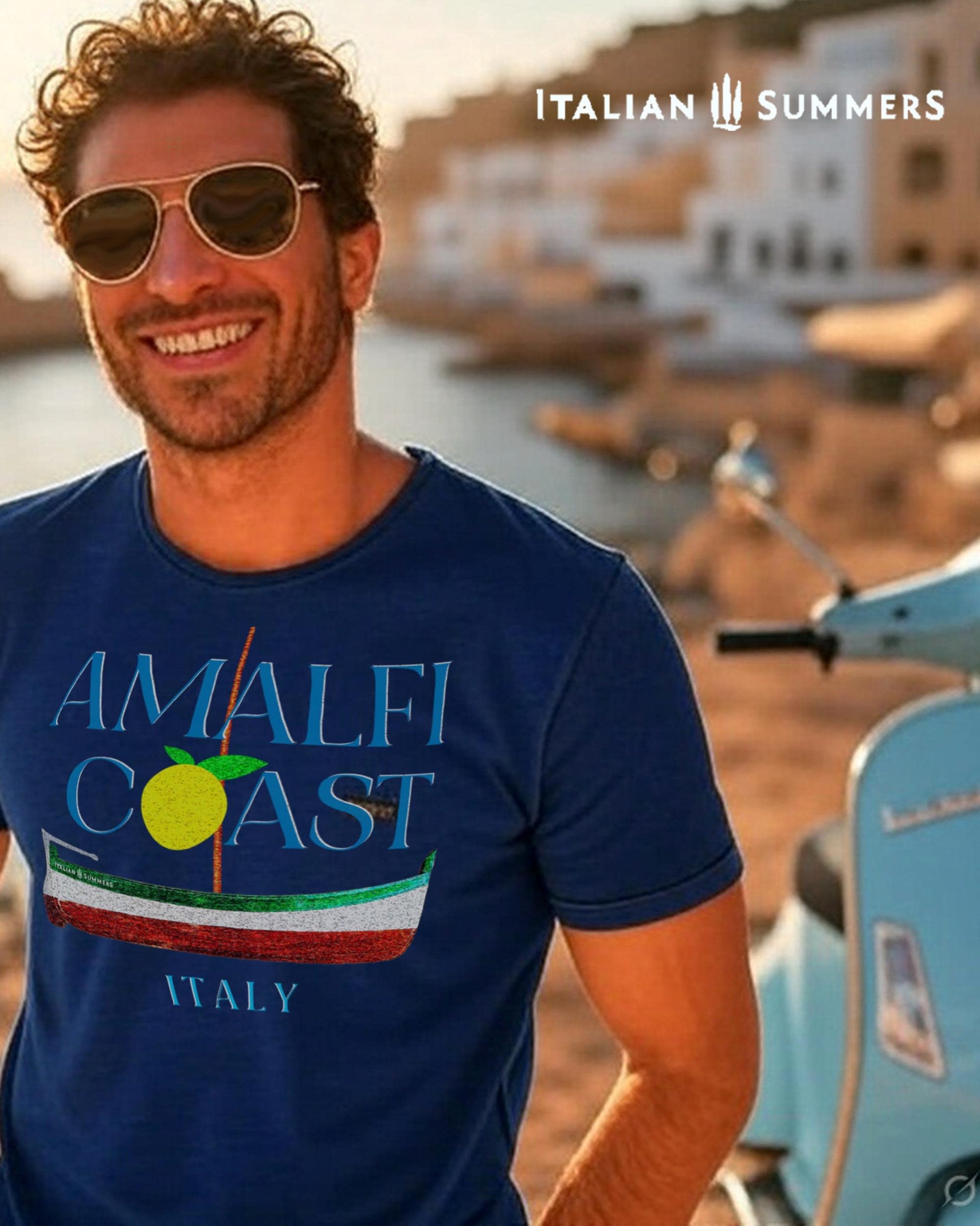 A smiling Italian man wearing a navy blue  T shirt with blue text: AMALFI COAST, the O in Coast is a yellow stylized lemon with two leaves.
Under the text is a traditional Amalfi coast boat called a Gozzo, in the traditional colors of the Italian flag, green, white, red.
The text ITALY in light blue ends the composition on the bottom.