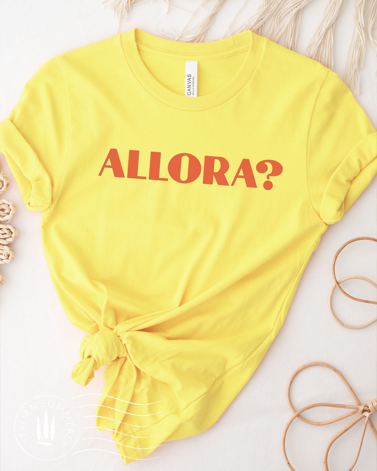 A yellow Italy inspired t-shirt with a red text of the the Italian expression: Allora?, Used all the time in Italian language. The color of the shirt is a soft pastel peach with the Allora expression in terra. Designed and sold by Italian Summers