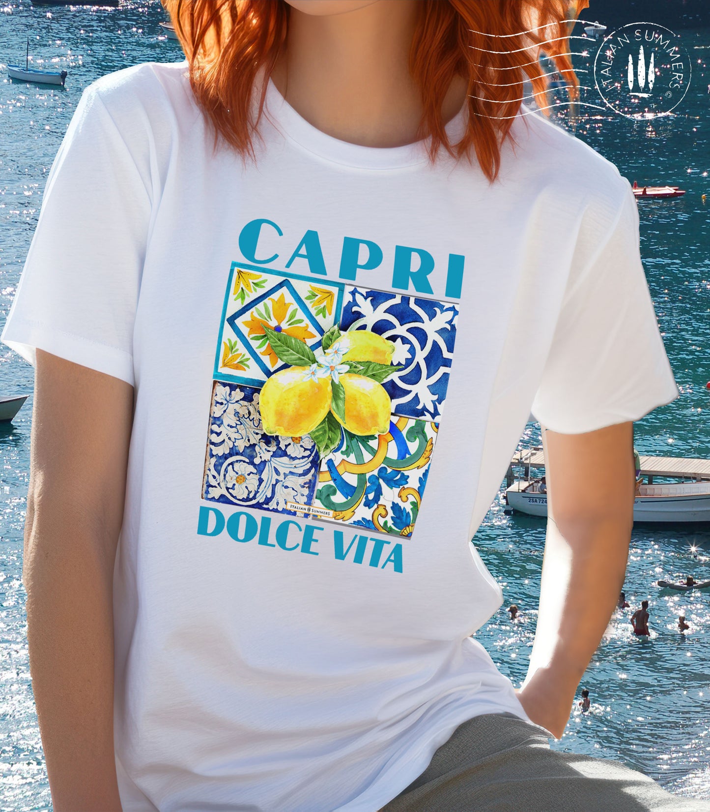 An all cotton T shirt with a Mediterranean tile design on the chest and a large cluster of Amalfi Coast lemons on top of the tiles. The lemons are bright yellow with green leaves and flowers. A blue text states: CAPRI DOLCE VITA