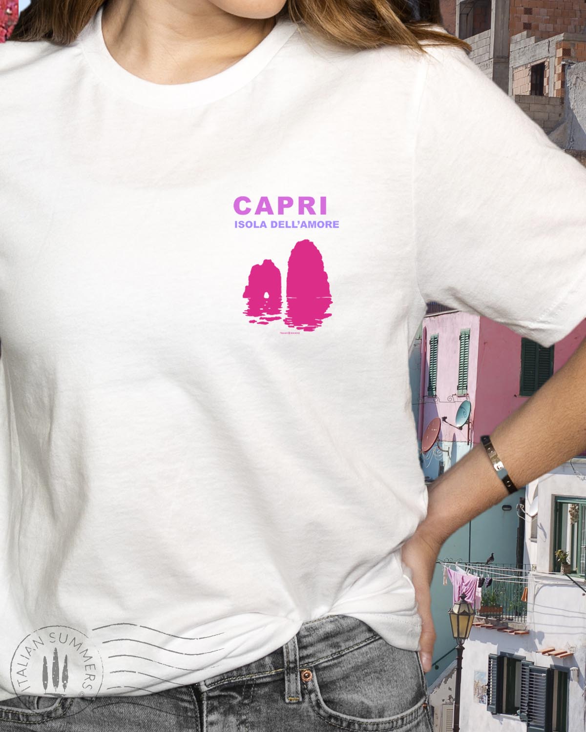 A youg woman stands in front of a quaint Italian island restaurant covered in pink bougainvilleas. She is standing with her back to us wearing a soft white cotton shirt with a pink and fuchsia print depicting the Faraglioni islets of the famous island of Capri. The text on the print states " Capri Isola dell'Amore" Capri, island of love.