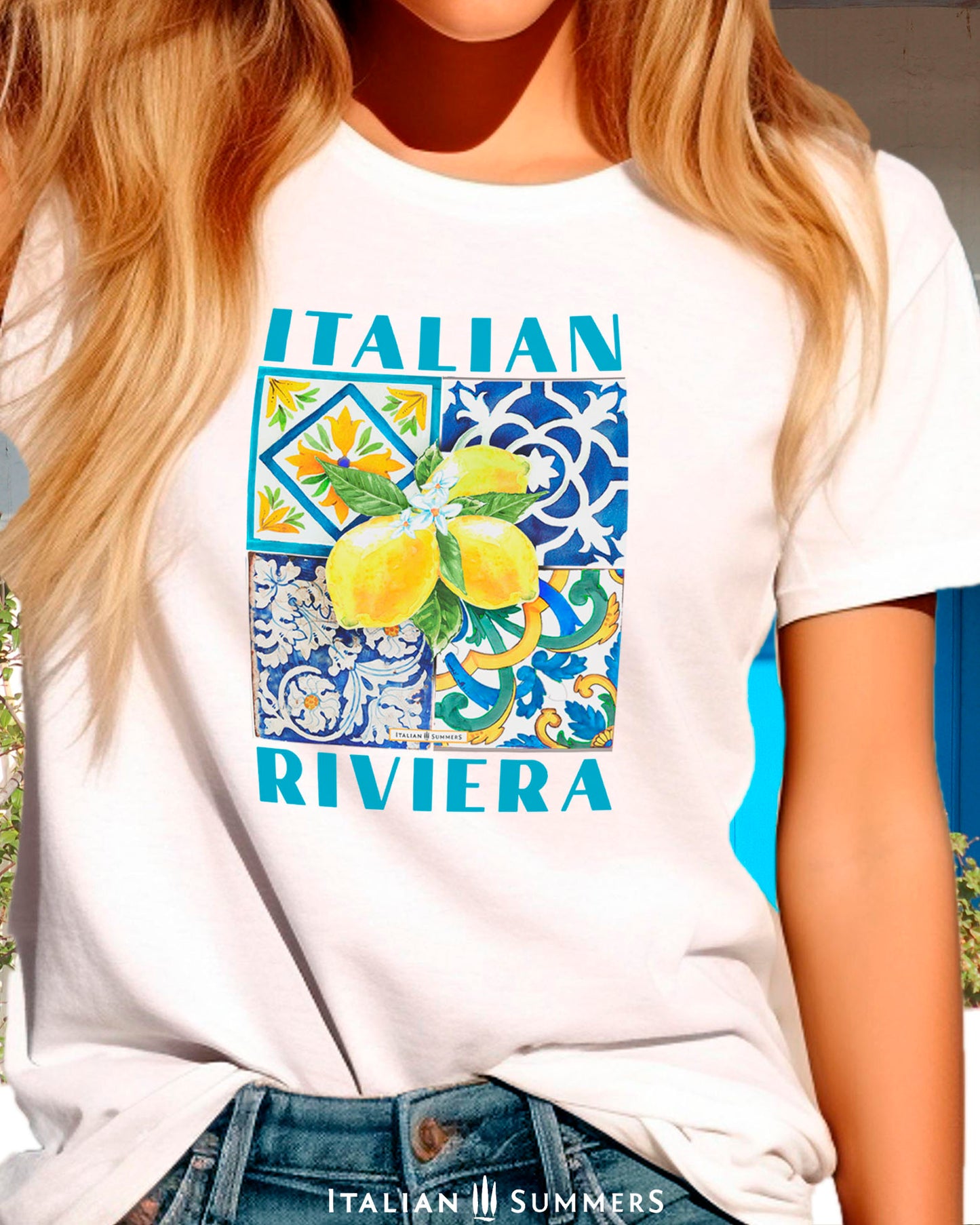 An all cotton T shirt with a Mediterranean tile design on the chest and a large cluster of Amalfi Coast lemons on top of the tiles. The lemons are bright yellow with green leaves and flowers. A blue text states: ITALIAN RIVIERA