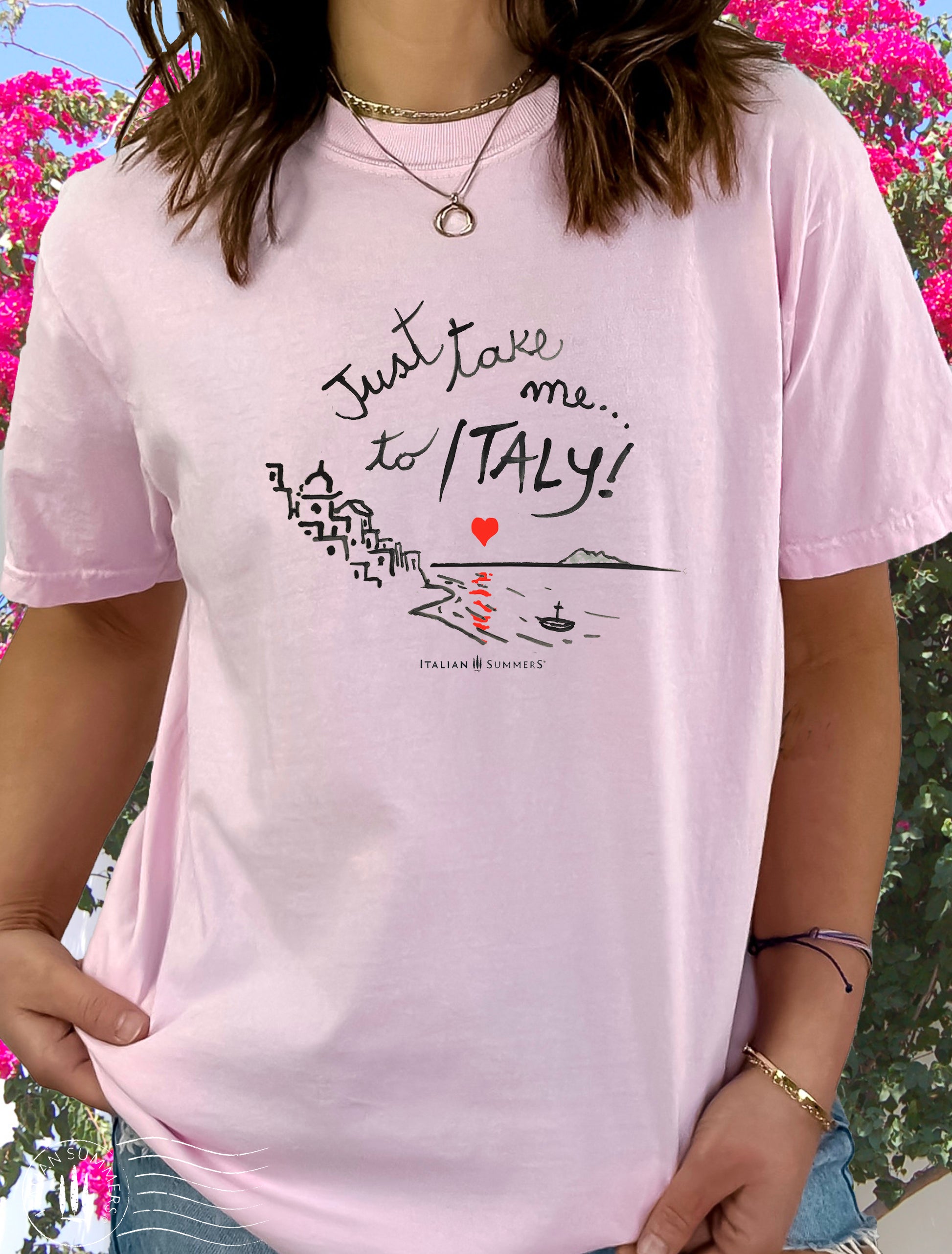 A girl is wearing a lItaly-inspired  pink Unisex crew neck T shirt with a print of a hand-painted  stylized Amalfi Coast village with a red heart setting on the sea and reflecting its glow on the waters. The hand-painted phrase "Just take me to Italy" is above the composition