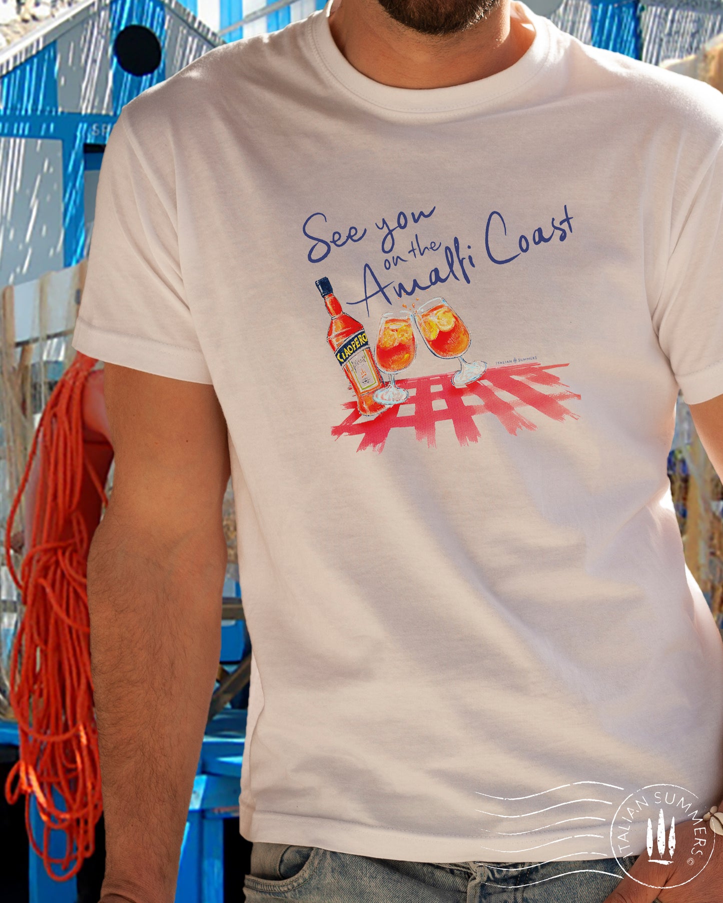 Italy inspired white t-shirt with the text See you on the Amalfi Coast in navy blue and a sketch in water color with an Aperol bottle and 2 glassis filled with Aperol Spritz on a bright red table cloth.