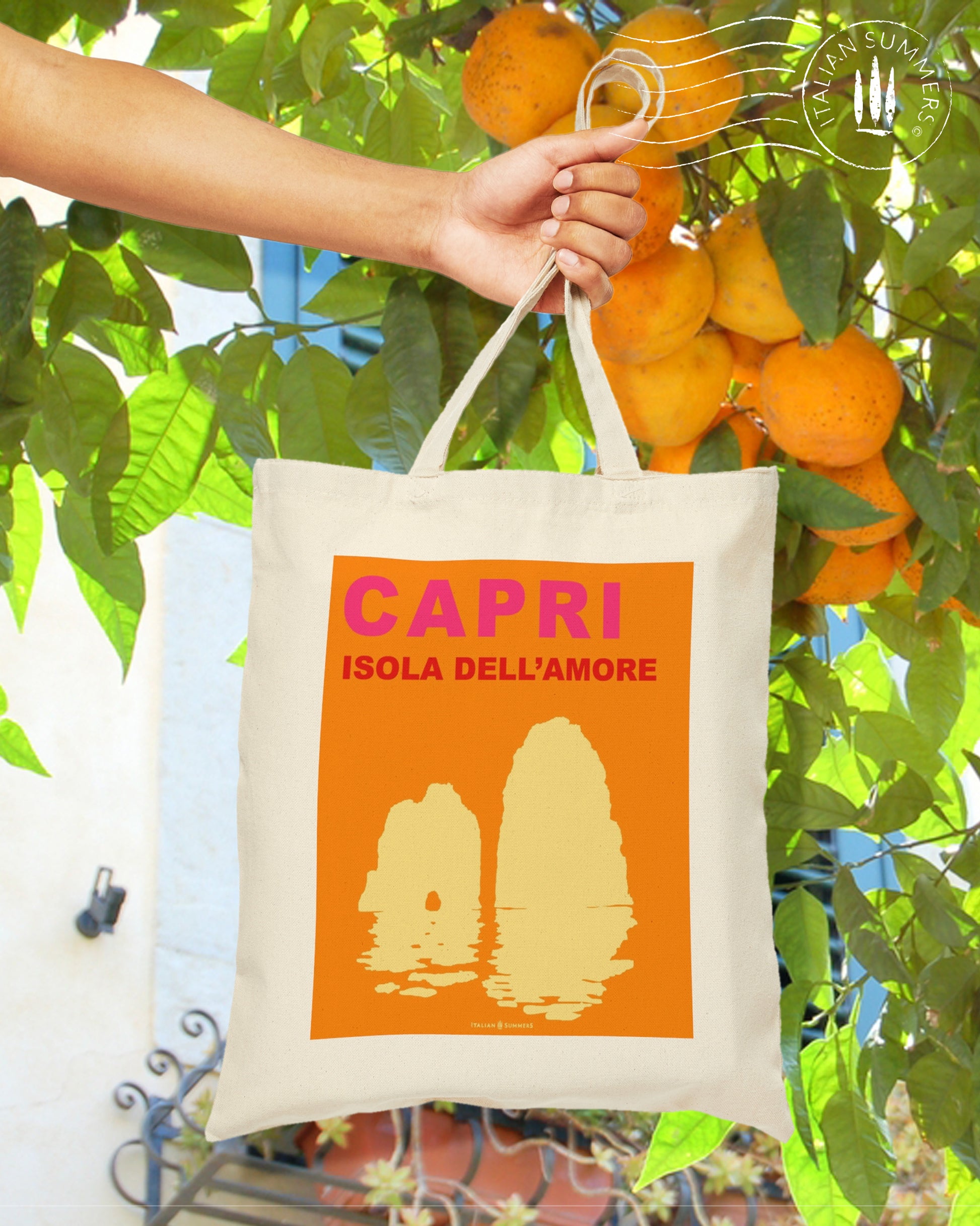 Italy inspired tote bag that represents an orange field containing a watm fuchsia Capri text and under that the text Isola del Amore means Isand of love. Under the text there is the silhouet of the Faraglioni in light warm color. Designed by Italian Summers