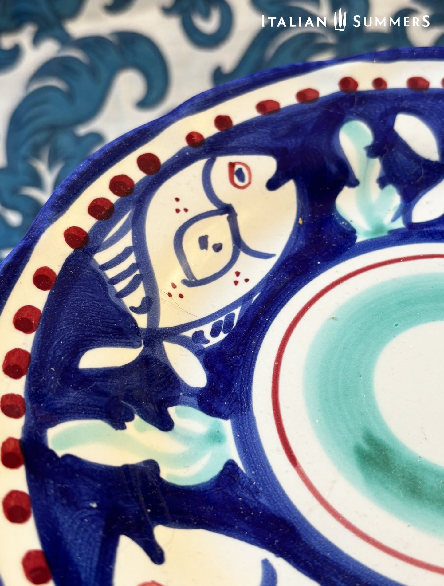 Zoomed-in view of a group of multi-Coloredl hand-painted Vietri Pasta Plates with fish theme decorations from the Amalfi Coast on a blue and white tablecloth