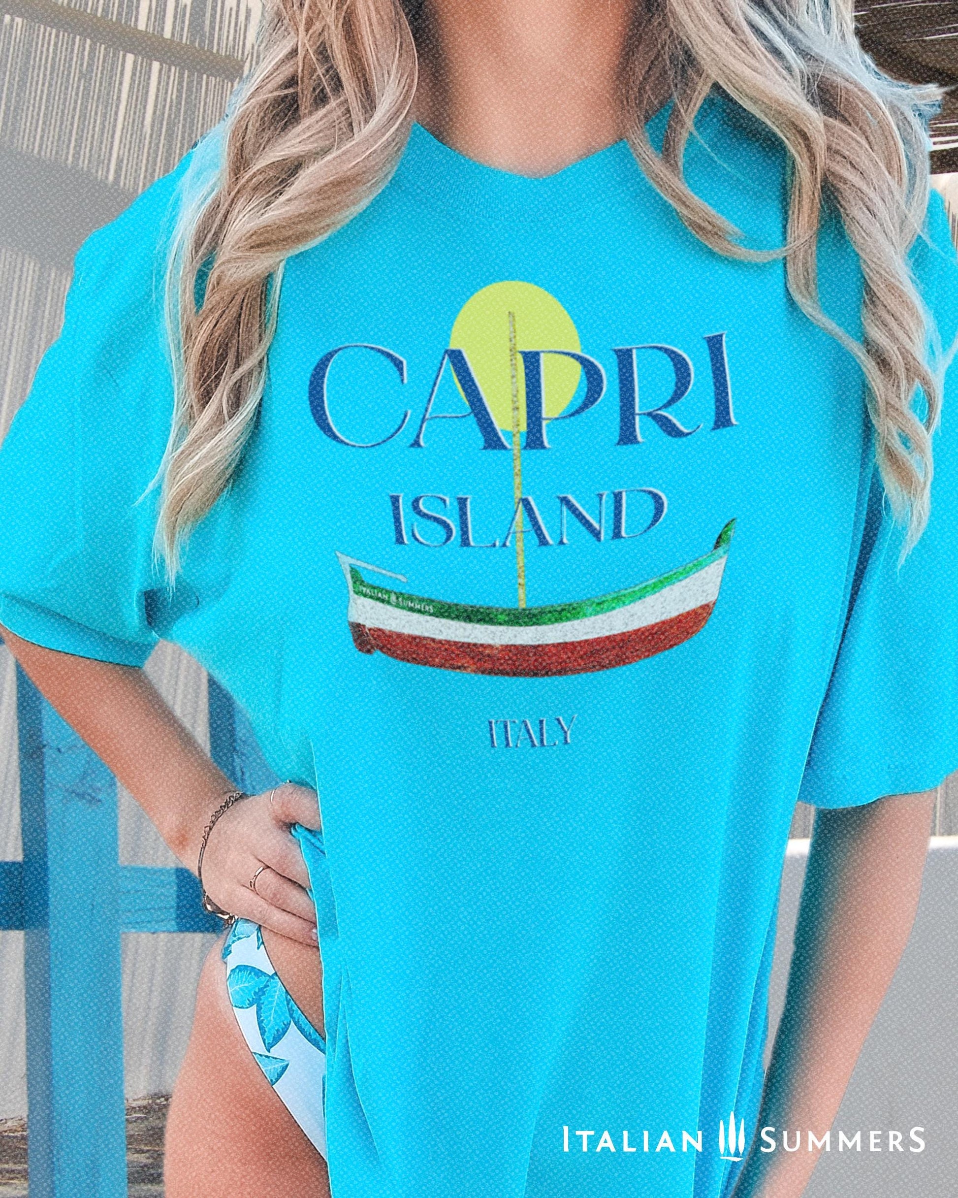 A Garment-dyed quality lagoon-blue T shirt with a print of a traditional Capri Island wooden boat in the color of the Italian flag, and the text CAPRI in capital letters above it, with a full-moon disk above.
