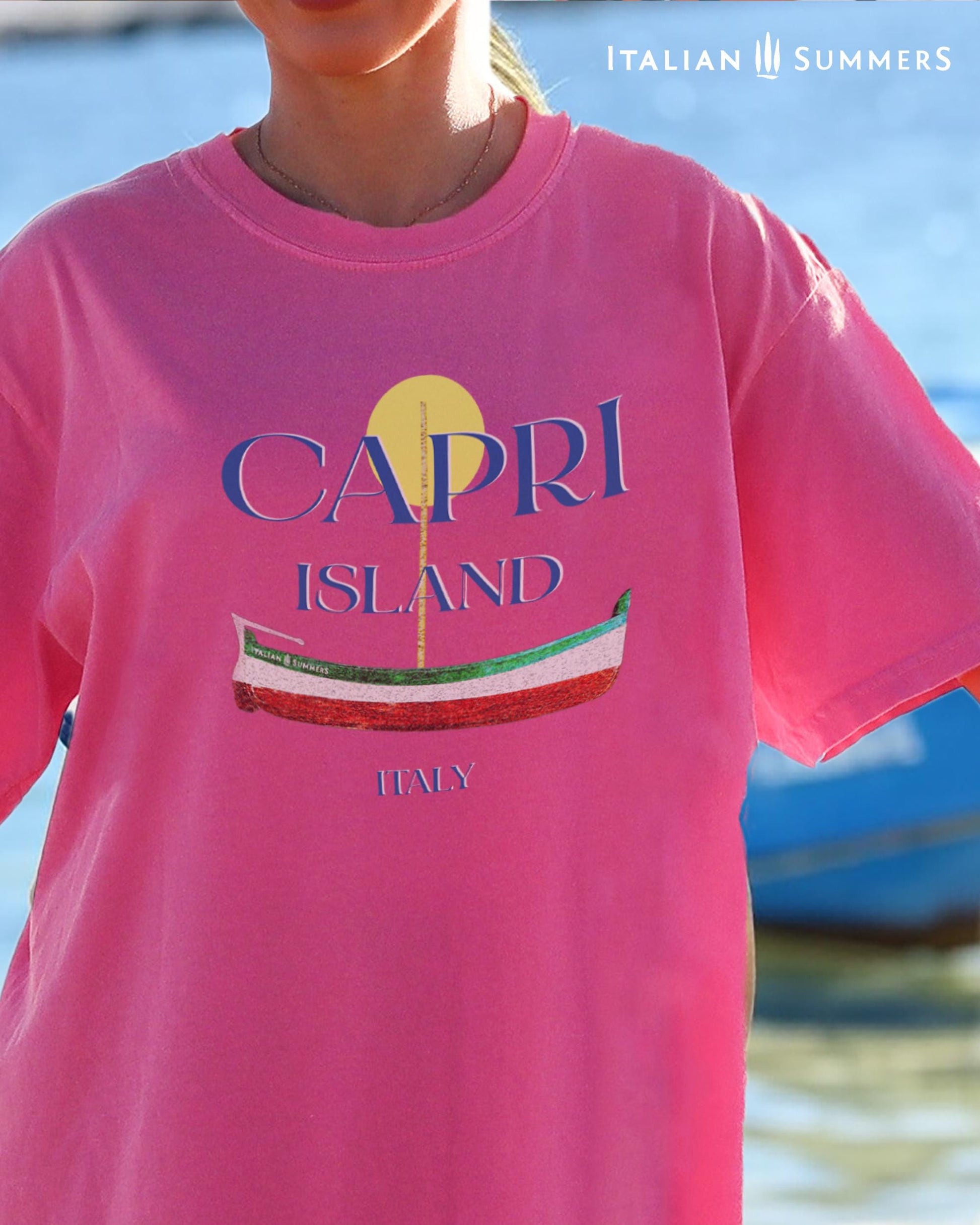 A Garment-dyed quality warm pinkT shirt with a print of a traditional Capri Island wooden boat in the color of the Italian flag, and the text CAPRI in capital letters above it, with a full-moon disk above.