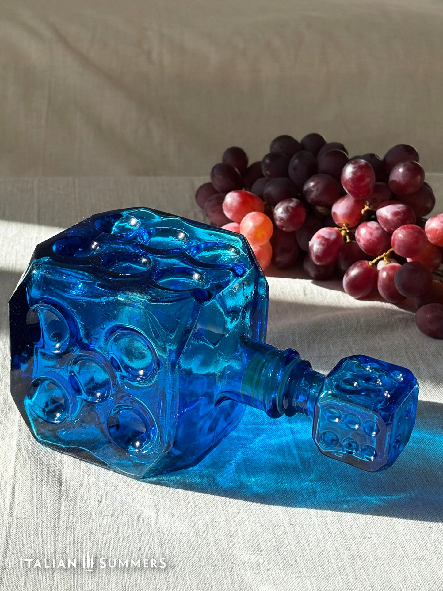 Sapphire blue Empoli dice glass decanter on a light background with red grapes