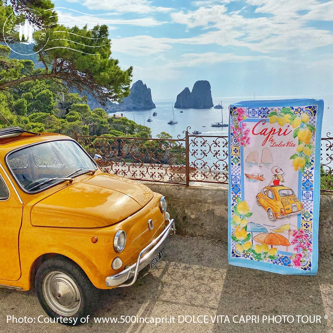 Italy inspired beach towel featuring a frame of colorful maiolica tiles and a view of a vintage yellow FIAT 500 car on Capri Island with a lady in a red dress with a large straw hat standing out of the car's sun roof and looking onto the Faraglioni. Made by Italian Summers. photo by www.500incapri.it