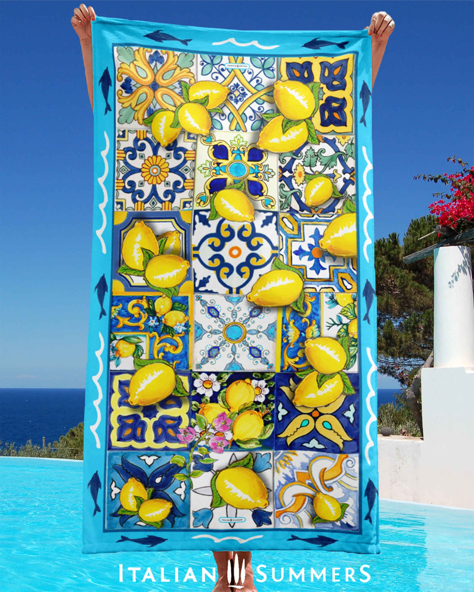 Beautiful Italy inspired beach towel printed with a turquoise rim with dolphins and a field of multi-colored italian maiolica tiles strewn with bunches of Sorrento lemons with flowers. Made by Italian Summers