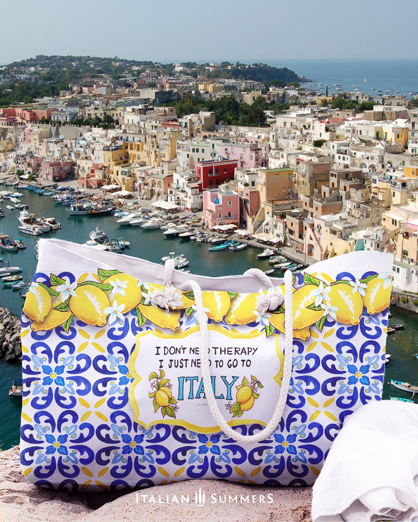 Italy inspired beach bag large model. It has the quote I don't need therapy, I just need to go to Italy. Next to the Italy writing a big Amalfi Coast lemons. The whole bag is printed with Italian tiles, colors blue with some yellow. On the rim of the bag there is a garland of lemons with lemon flowers. The quote with theblemons is placed on a white crest, and the crest is placed in the tile background. The Italy beach bag has soft rope handles. 