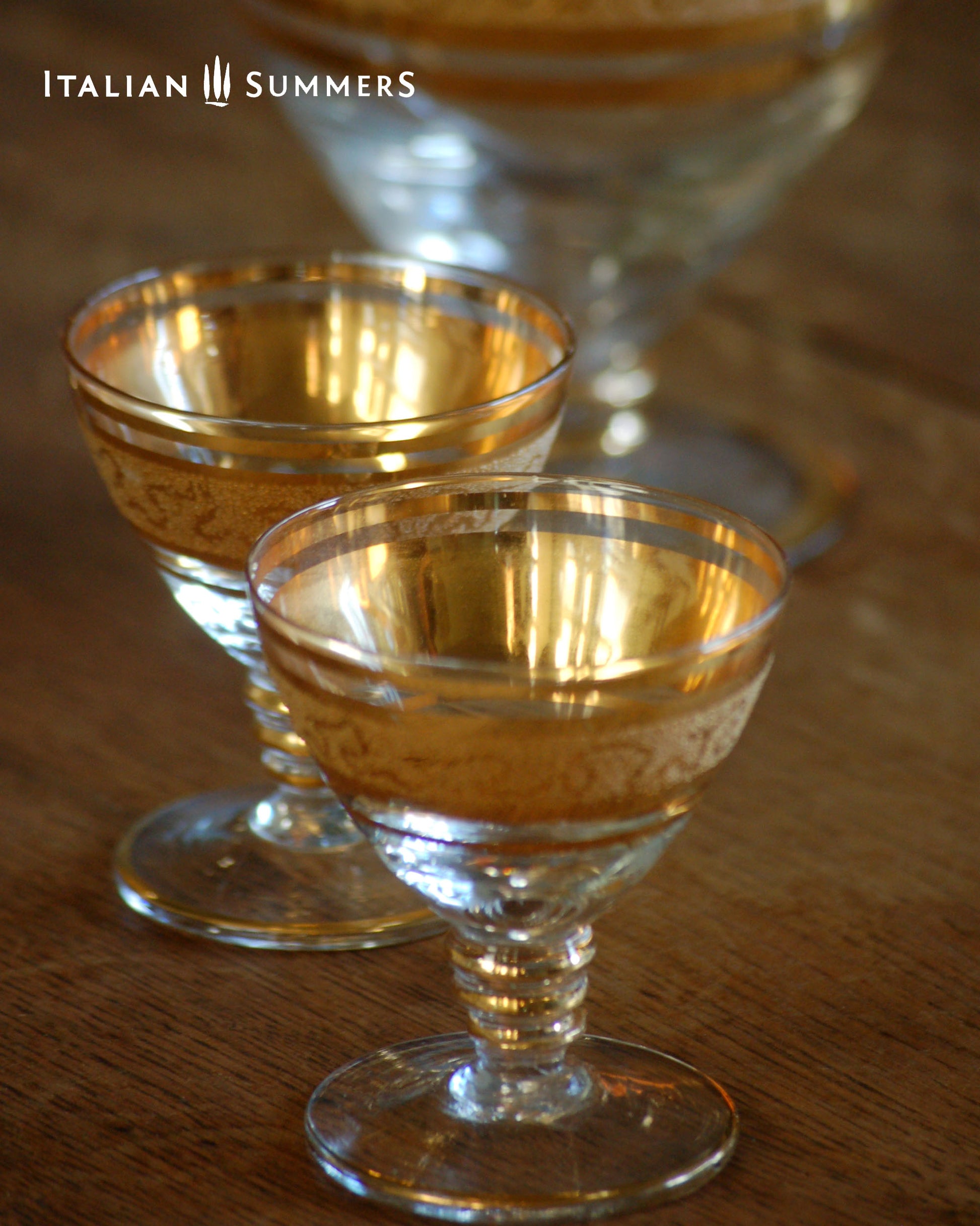 Two glass goblets with gold rims on a wooden surface, featuring the brand 'Italian Summers'.