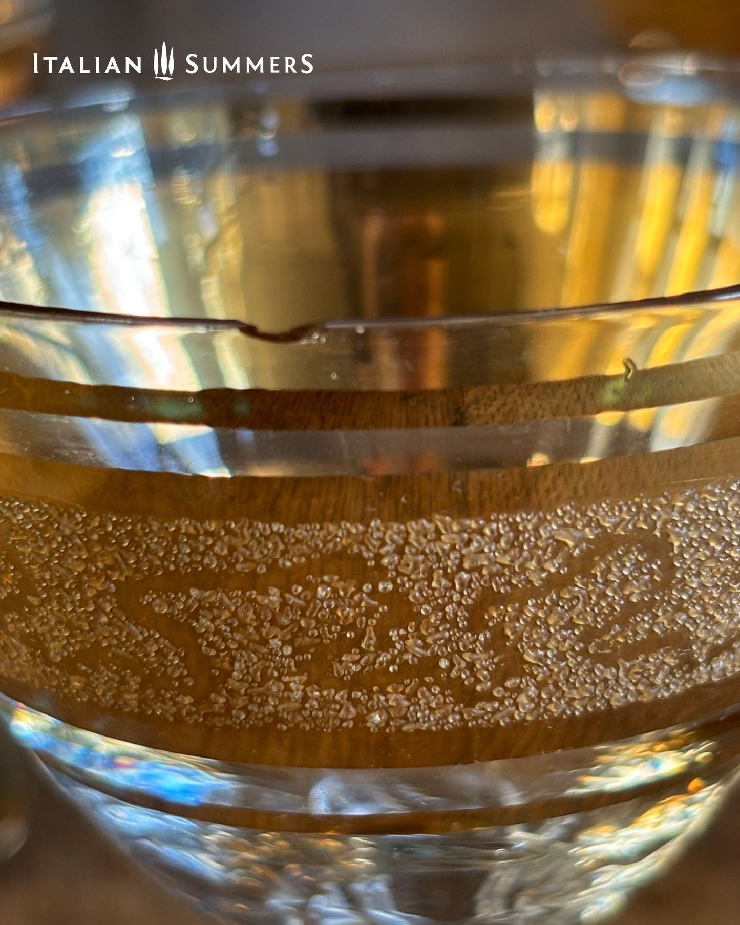 Close-up of a glass with embossed  gold design and 'Italian Summers' branding.