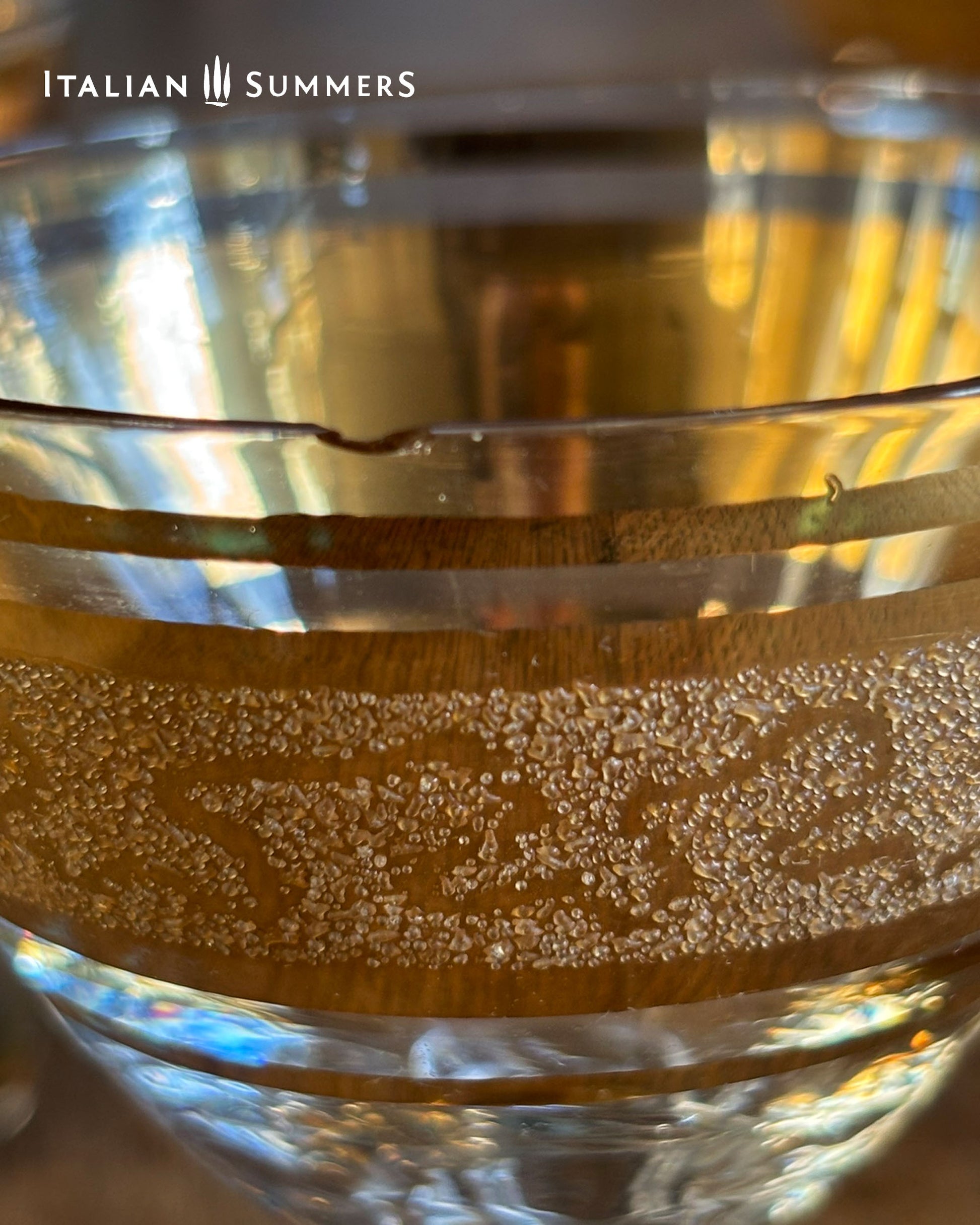 Close-up of a glass with embossed  gold design and 'Italian Summers' branding.