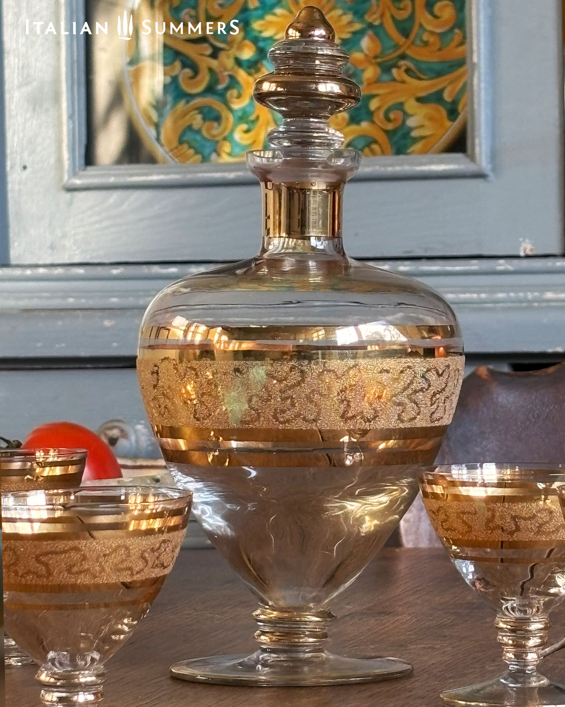 Decorative glass decanter and goblets with gold accents on a table.