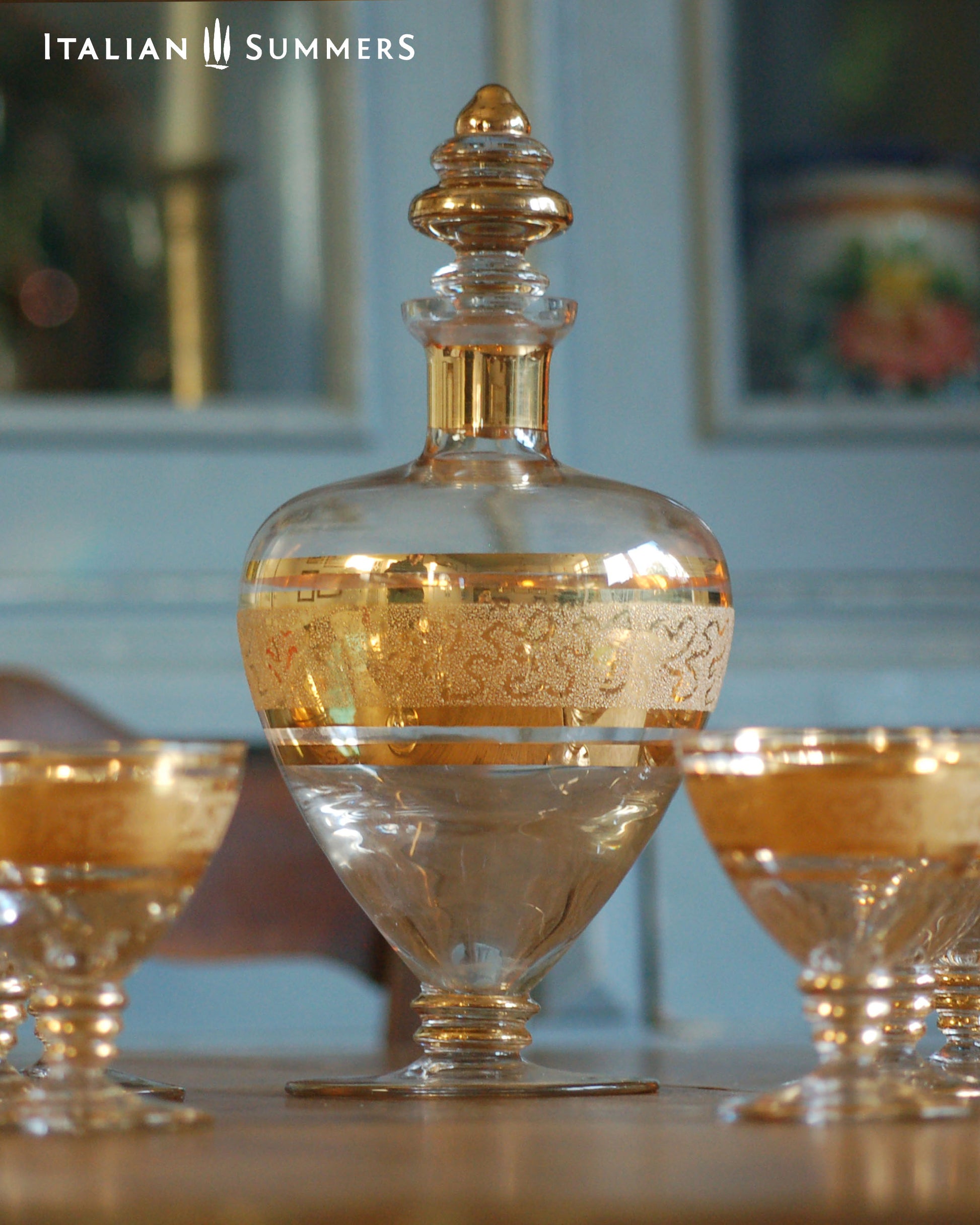 Decorative glass decanter with gold accents on a table, with 'Italian Summers' branding.